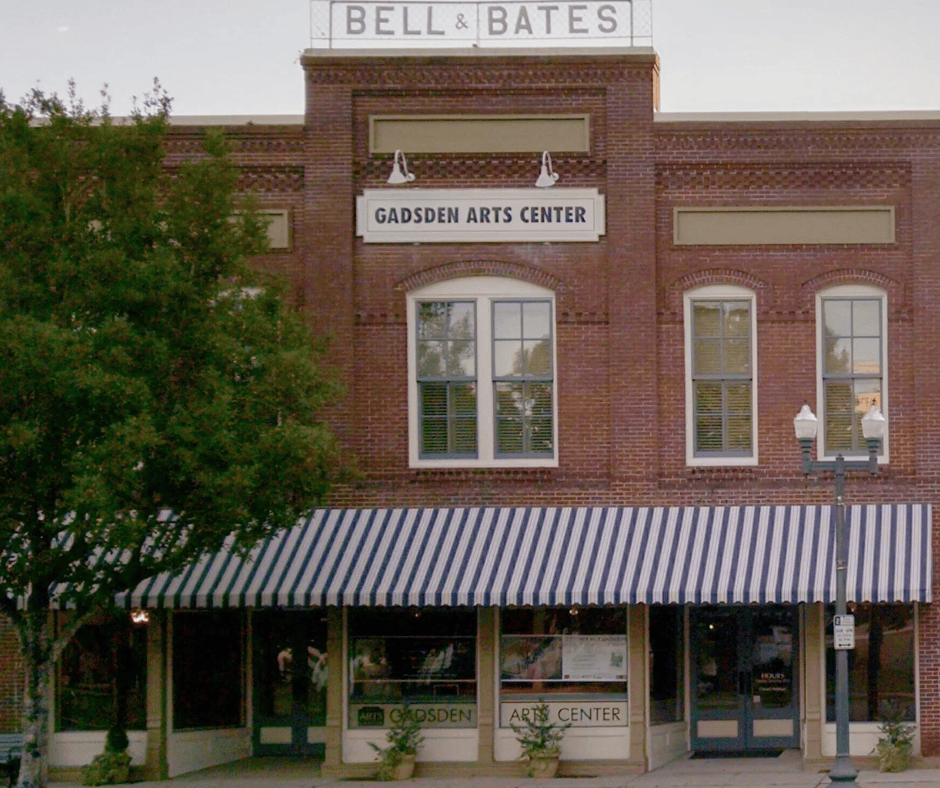 Brick storefront for Bell & Bates, with Gadsden Arts Center sign and striped awning under trees