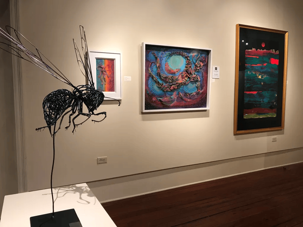 Gallery wall with three framed artworks and a black spider sculpture on a white pedestal