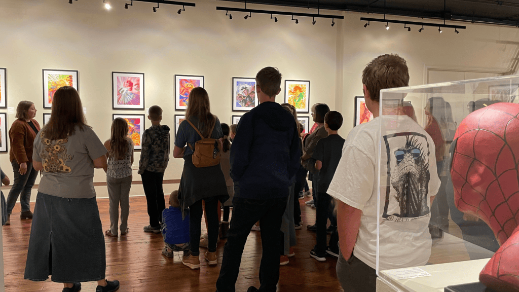 Visitors viewing colorful artwork in a gallery, with a Spider-Man display on the right.