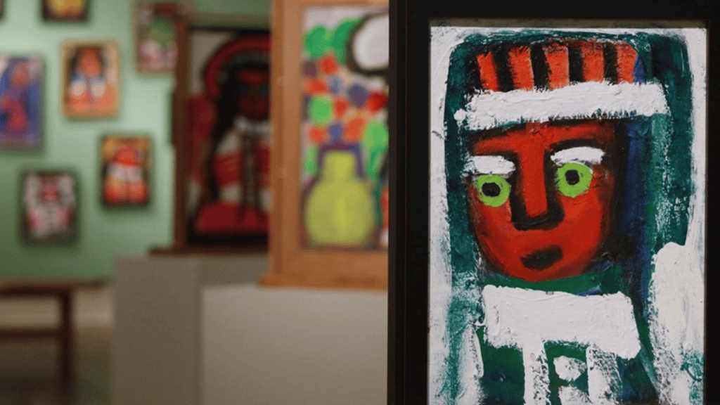 Art gallery with colorful framed works, including a close-up painting of a red-faced figure on the right.
