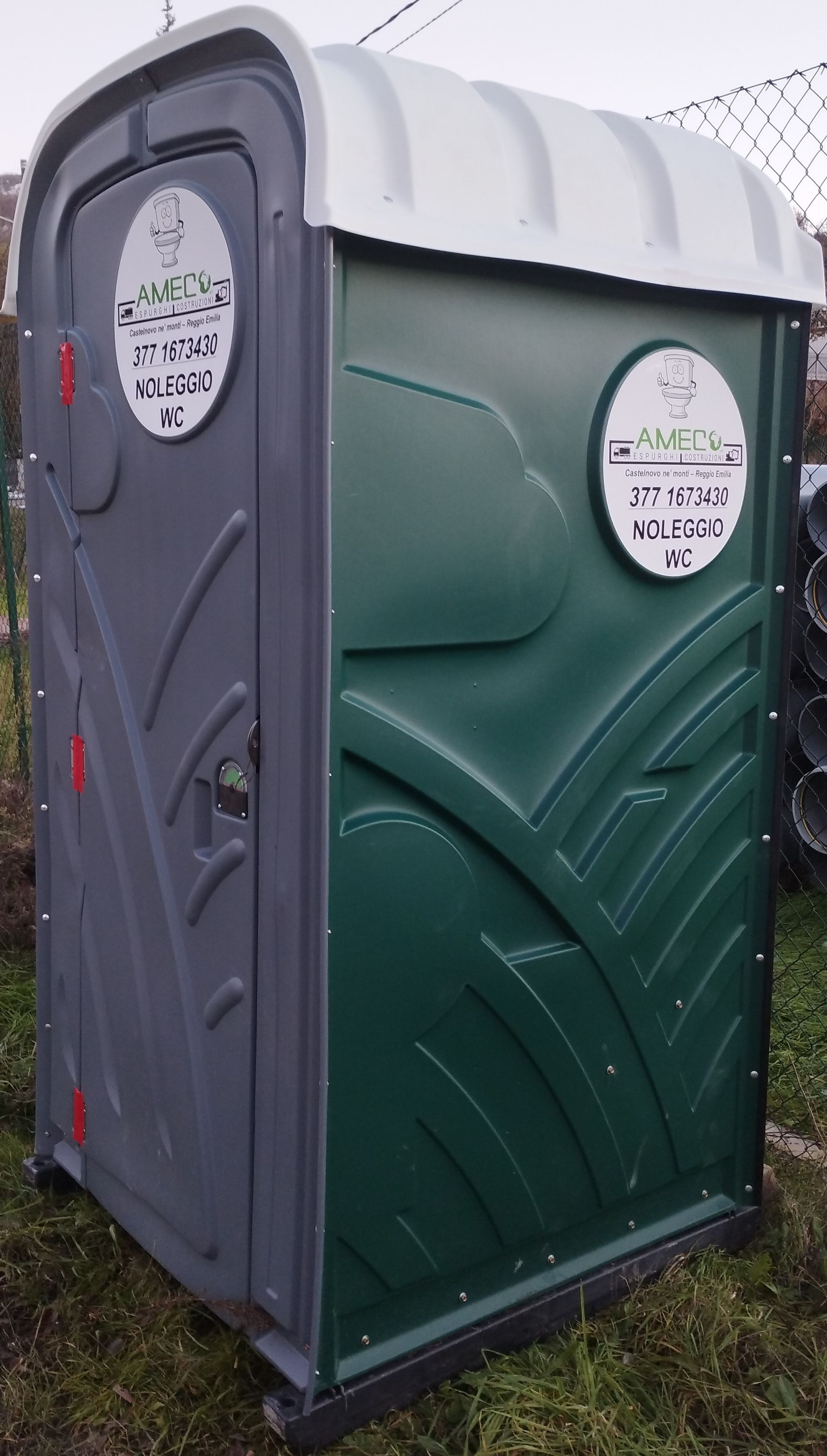 Un bagno chimico di Ameco verde e grigio è appoggiato sull'erba.