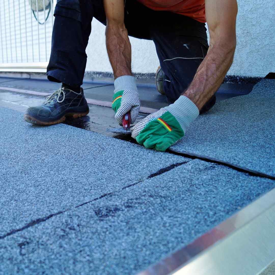 Worker in gloves securing blue roof shingles on a rooftop.