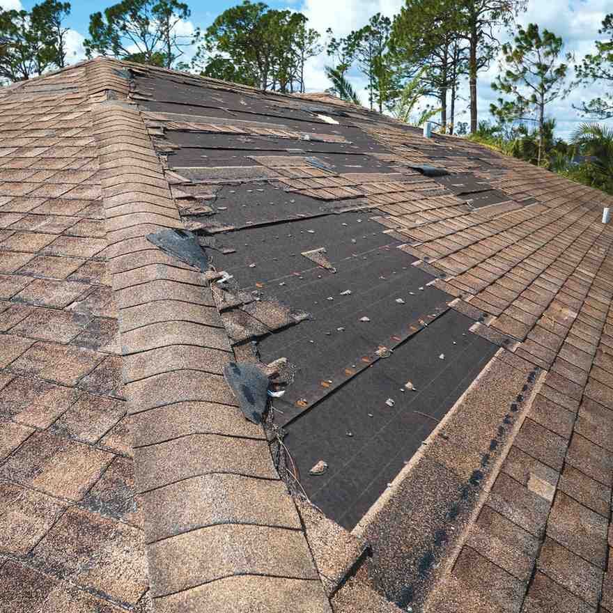 Damaged shingle roof with exposed black underlayment and missing shingles on a house