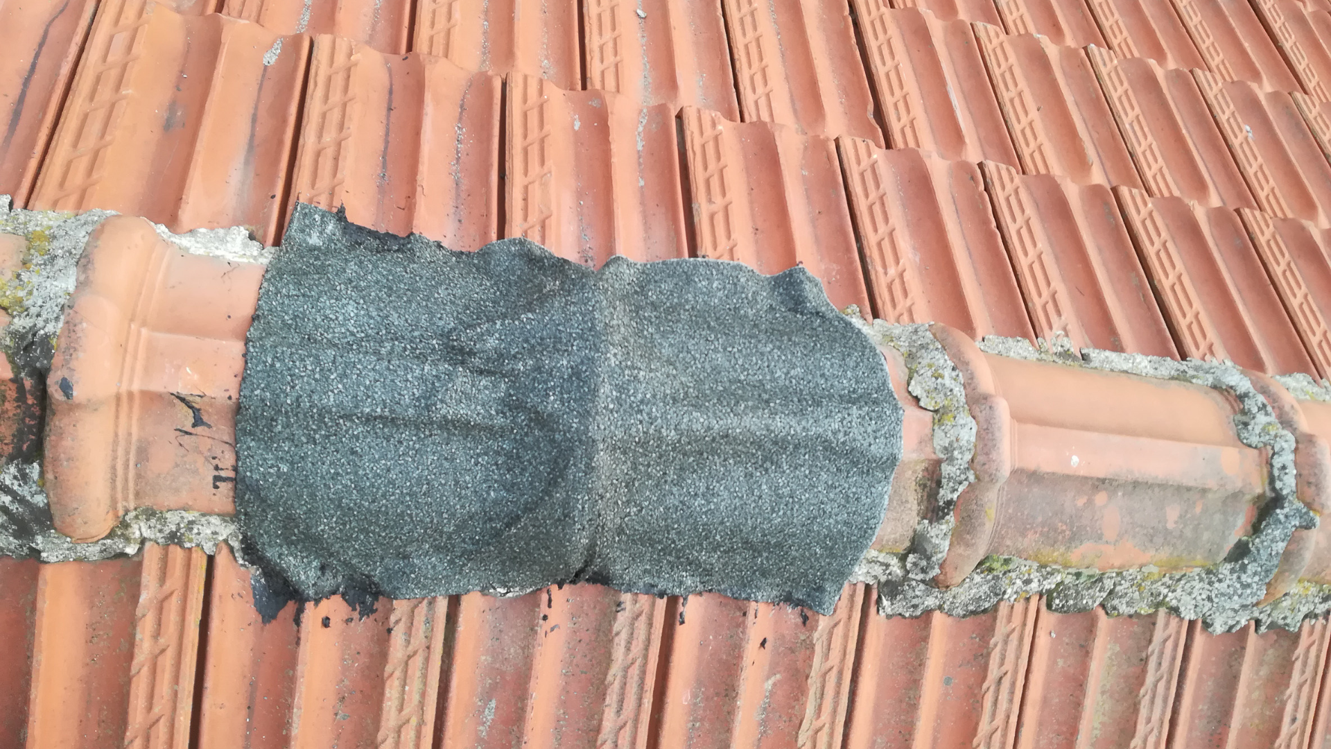 Damaged roof pipe flashing patched with dark sealant on terracotta roof tiles