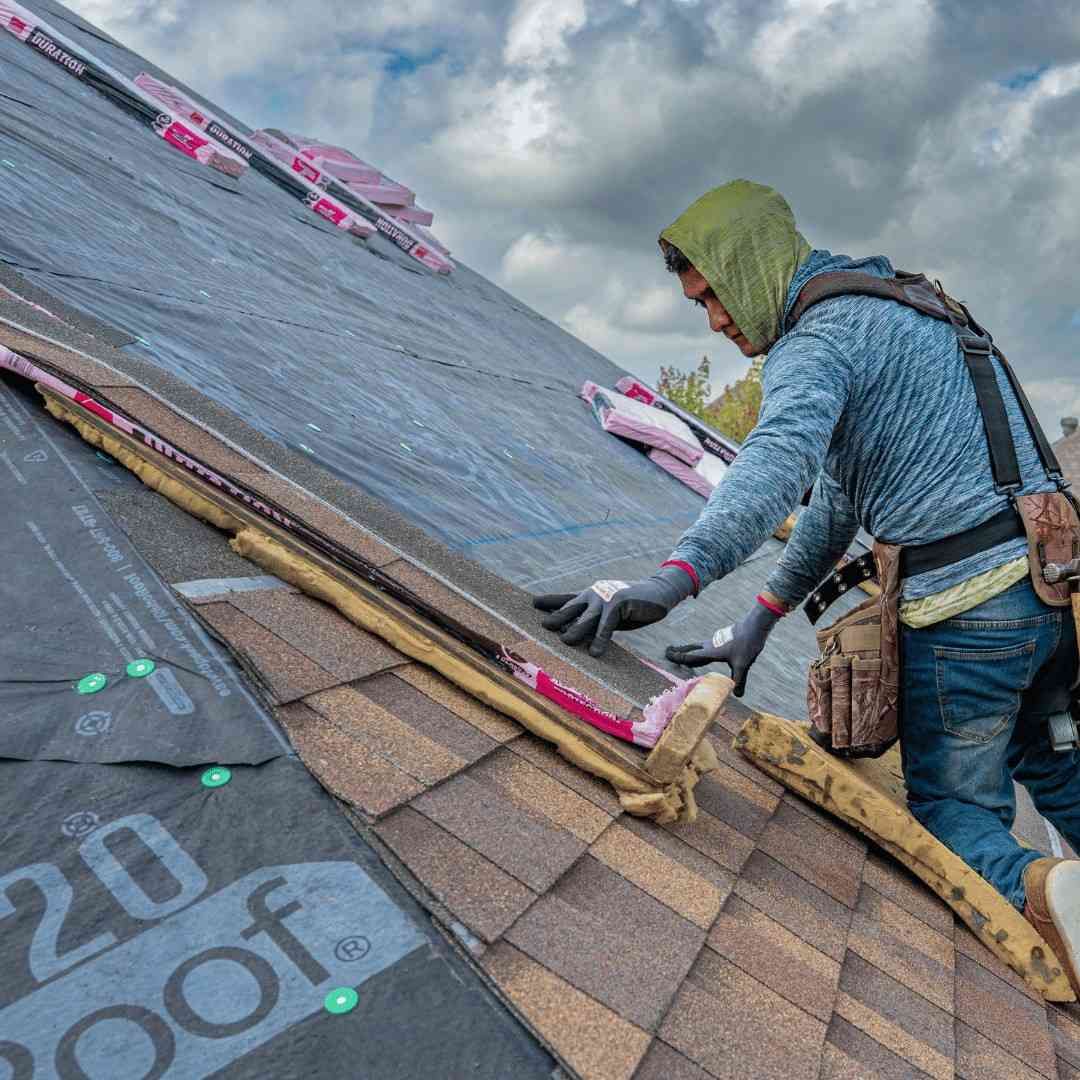 Roofer installing underlayment on a sloped shingle roof under cloudy skies