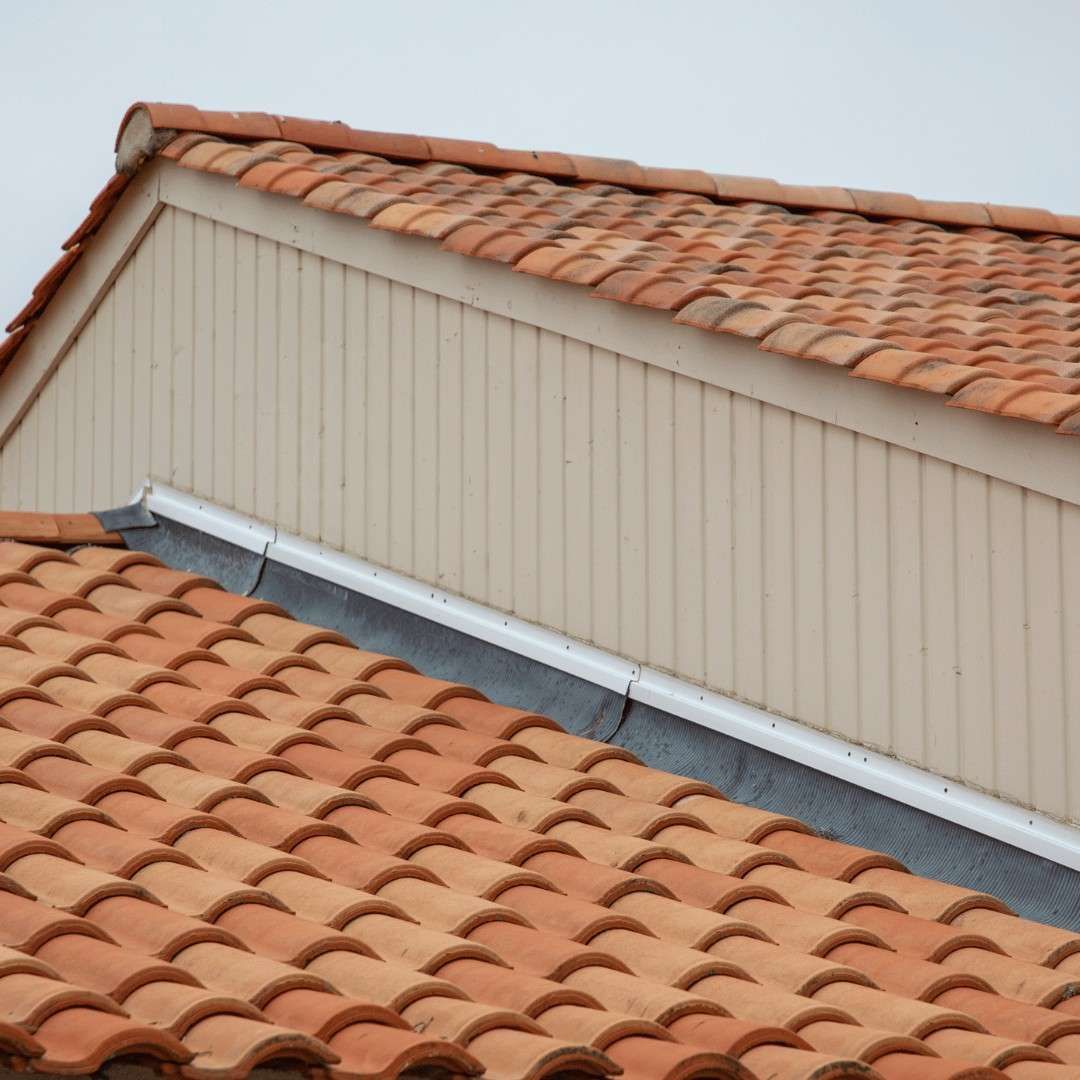 Terracotta tile roofs with a beige dormer wall and gray metal flashing against a white sky