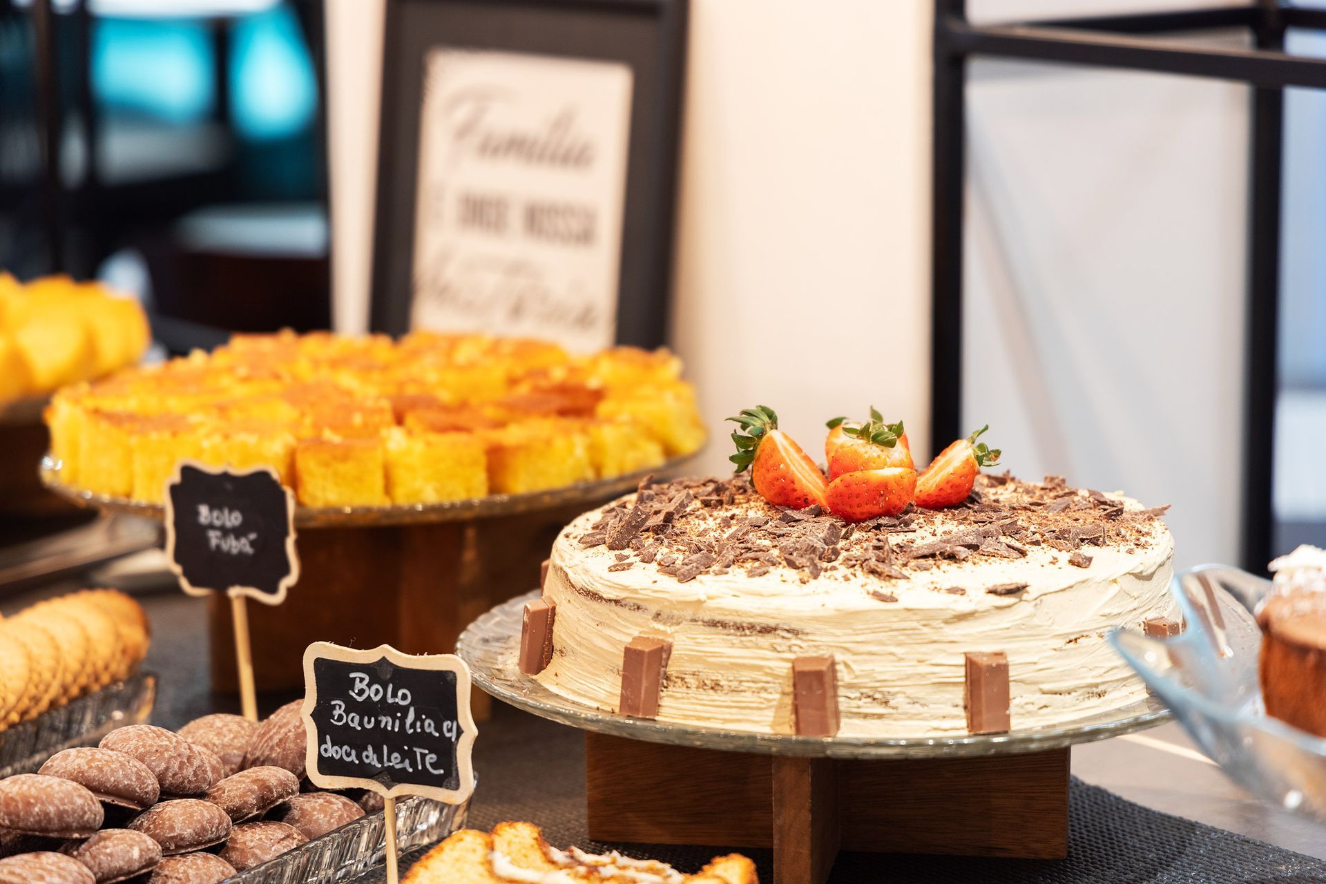 Buffet de sobremesas com doces e um bolo coberto com morangos sobre uma mesa expositora