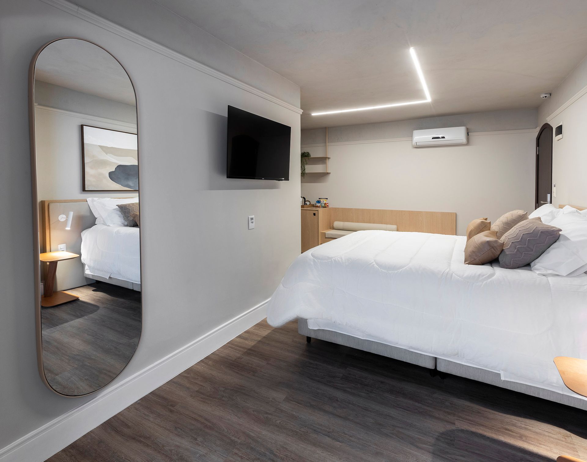 Quarto moderno com cama king size, TV montada na parede, espelho de corpo inteiro, paredes cinzentas e piso de madeira escura