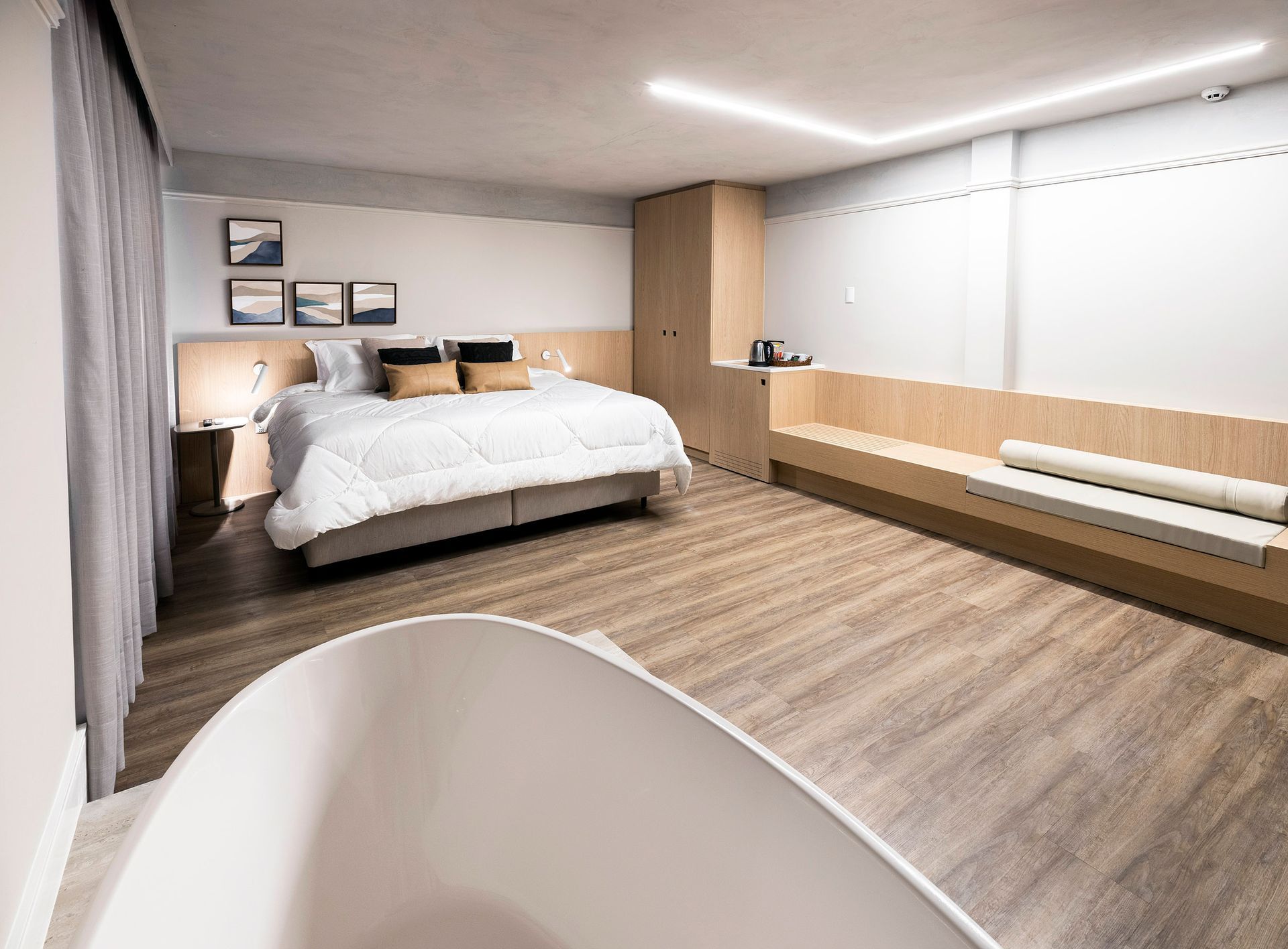 Quarto moderno com uma cama grande, piso de madeira, escrivaninha embutida e banheira branca em primeiro plano