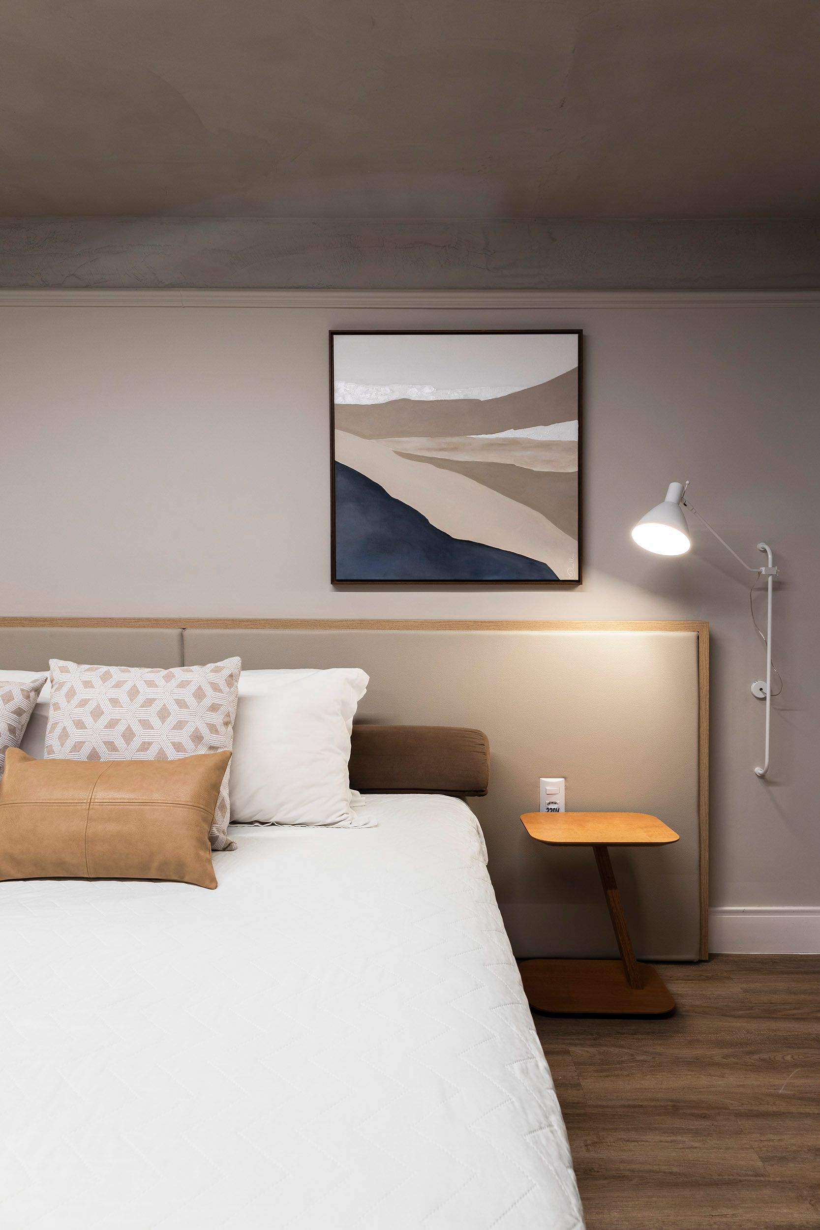 Quarto minimalista com roupa de cama branca, quadros emoldurados e um candeeiro de pé ao lado da cama.