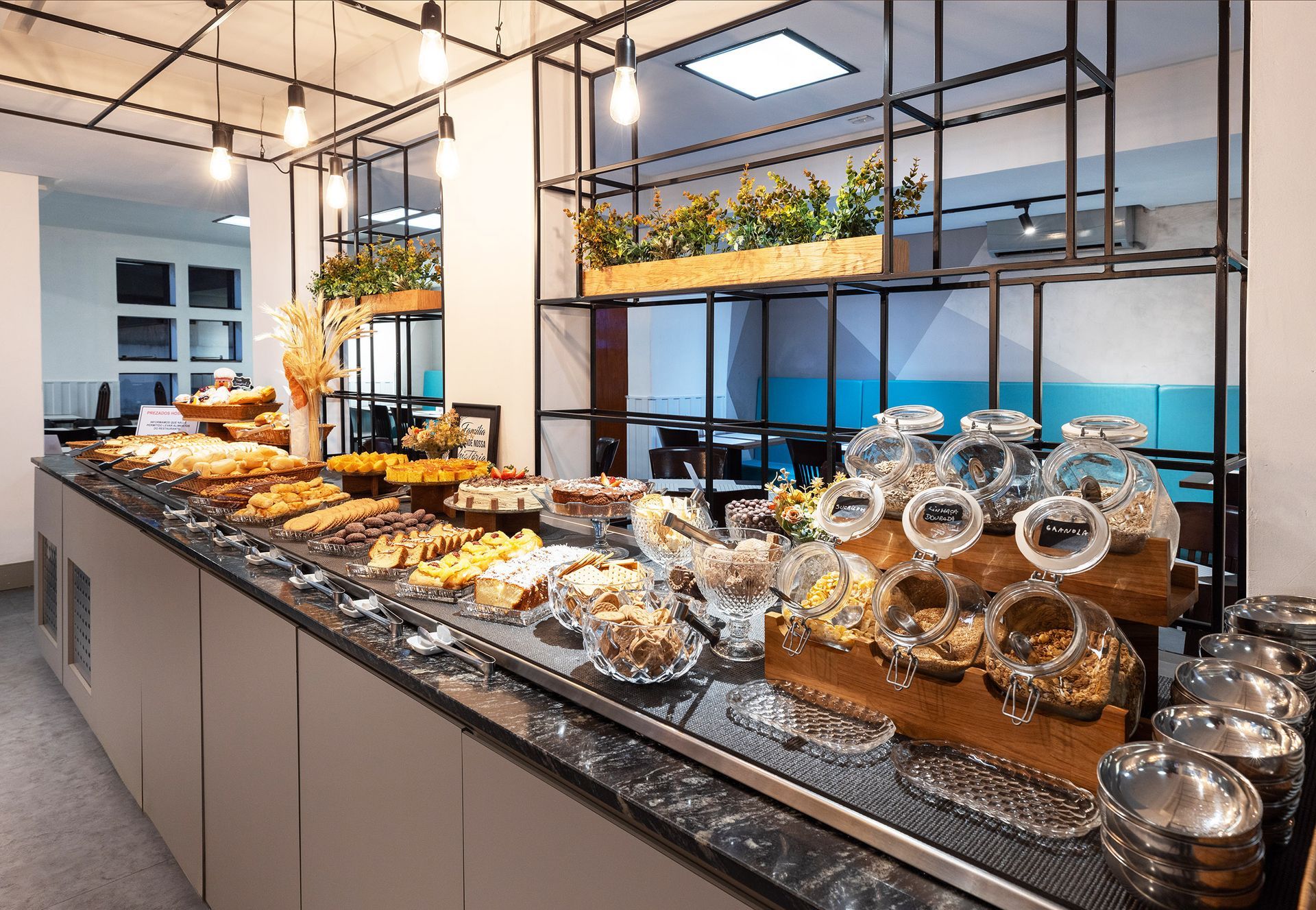 Balcão de buffet moderno com pão, doces, potes e luminárias pendentes em uma sala de jantar bem iluminada