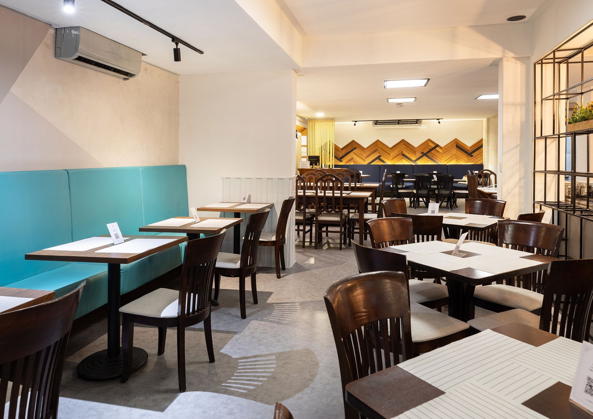 Café moderno vazio, com mesas brancas, cadeiras pretas, banco corrido turquesa e balcão ao fundo com iluminação aconchegante