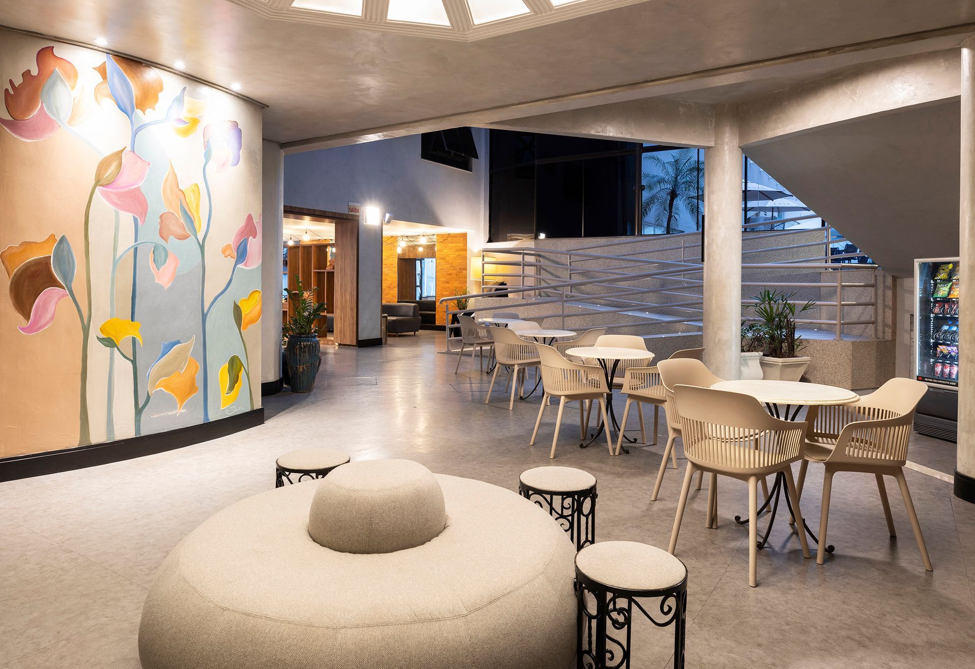 Interior de café moderno com mural em tons pastel, mesas redondas, banquetas e um banco curvo para lounge