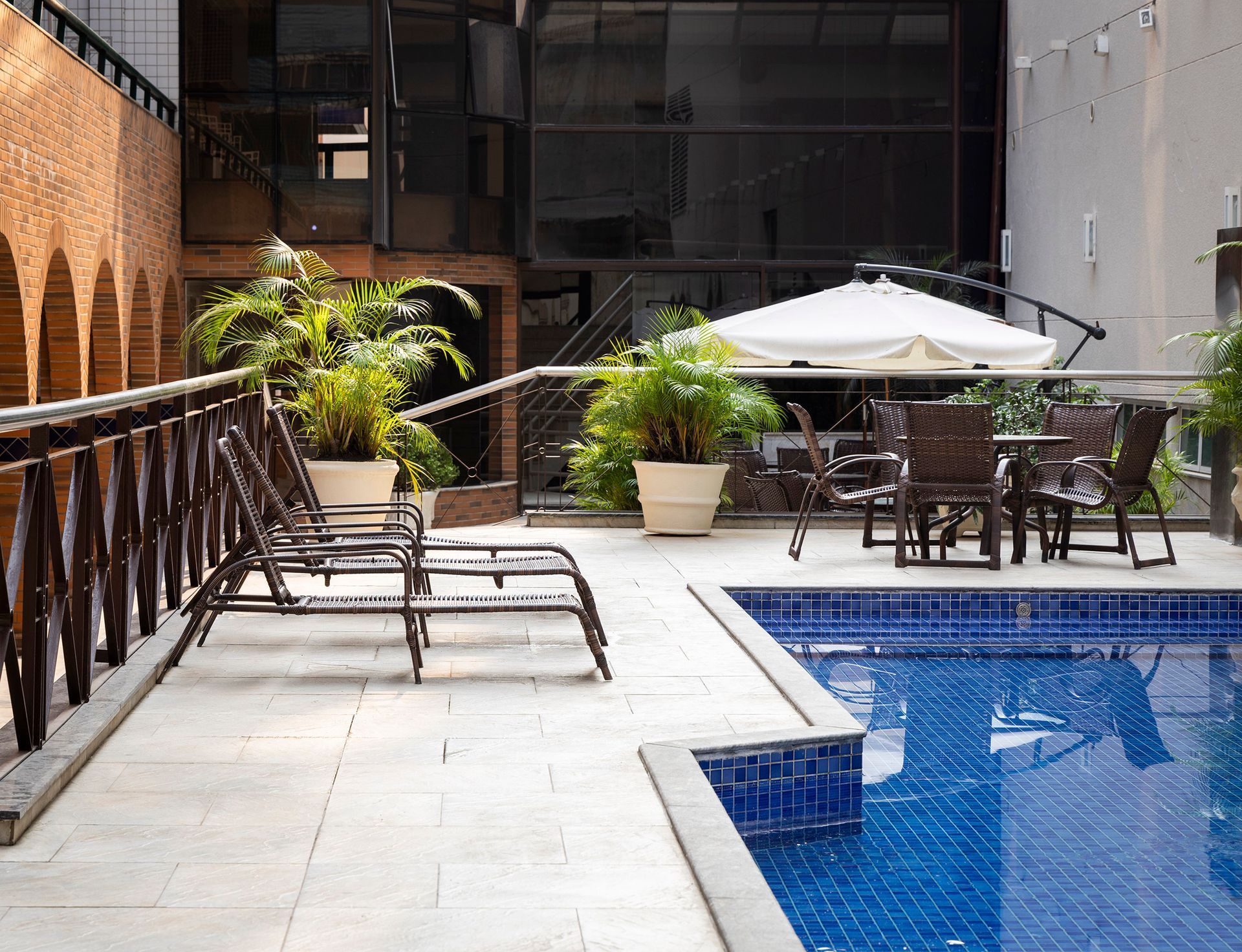 Piscina no pátio com espreguiçadeiras, plantas em vasos e mesas ao ar livre sob guarda-sóis