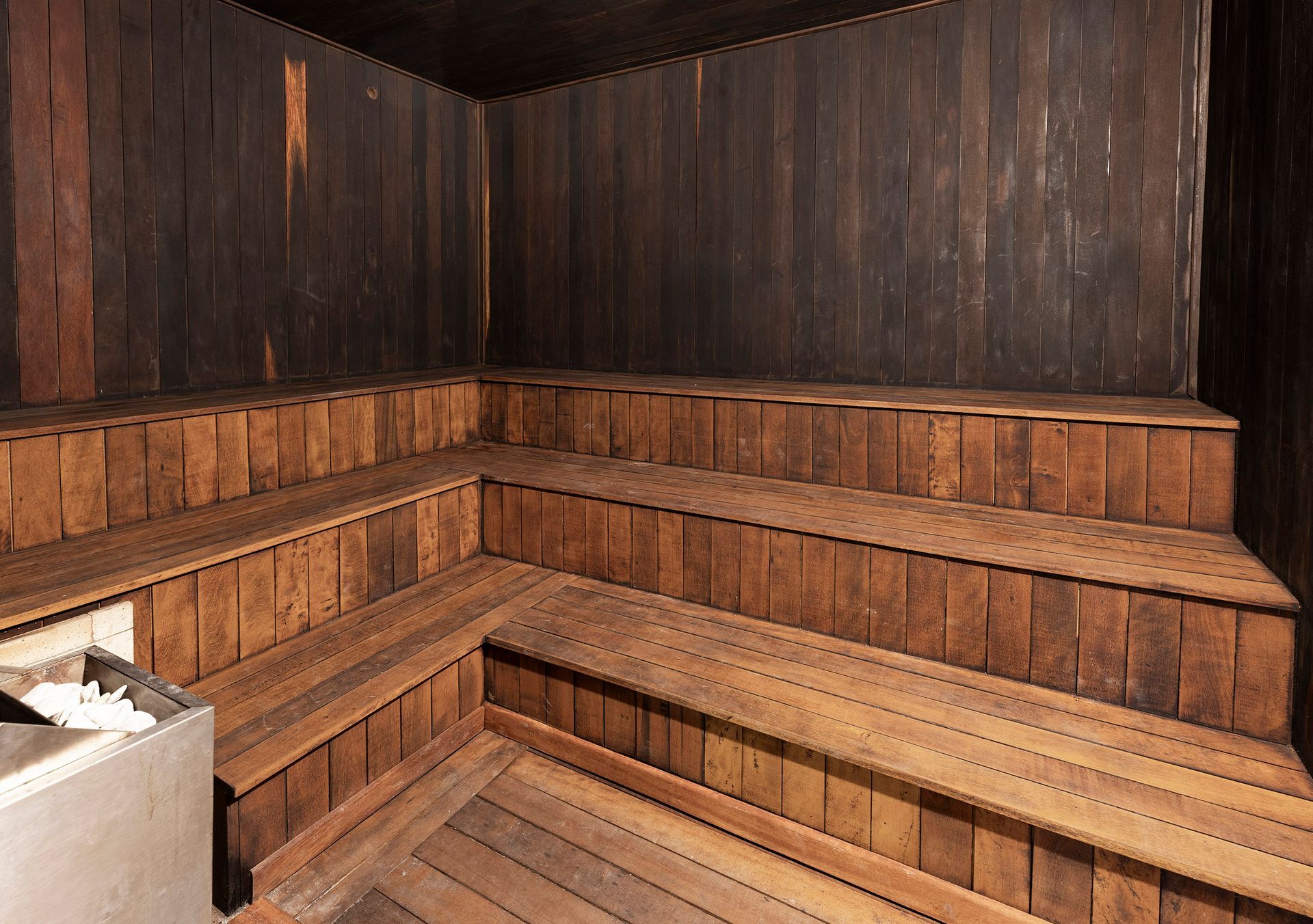 Sauna revestida de madeira, com bancos de madeira em vários níveis e uma lixeira no canto