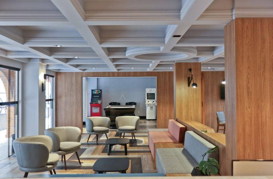 Sala de estar moderna com cadeiras cinzentas, um sofá, paredes revestidas de madeira e um teto branco com caixotões