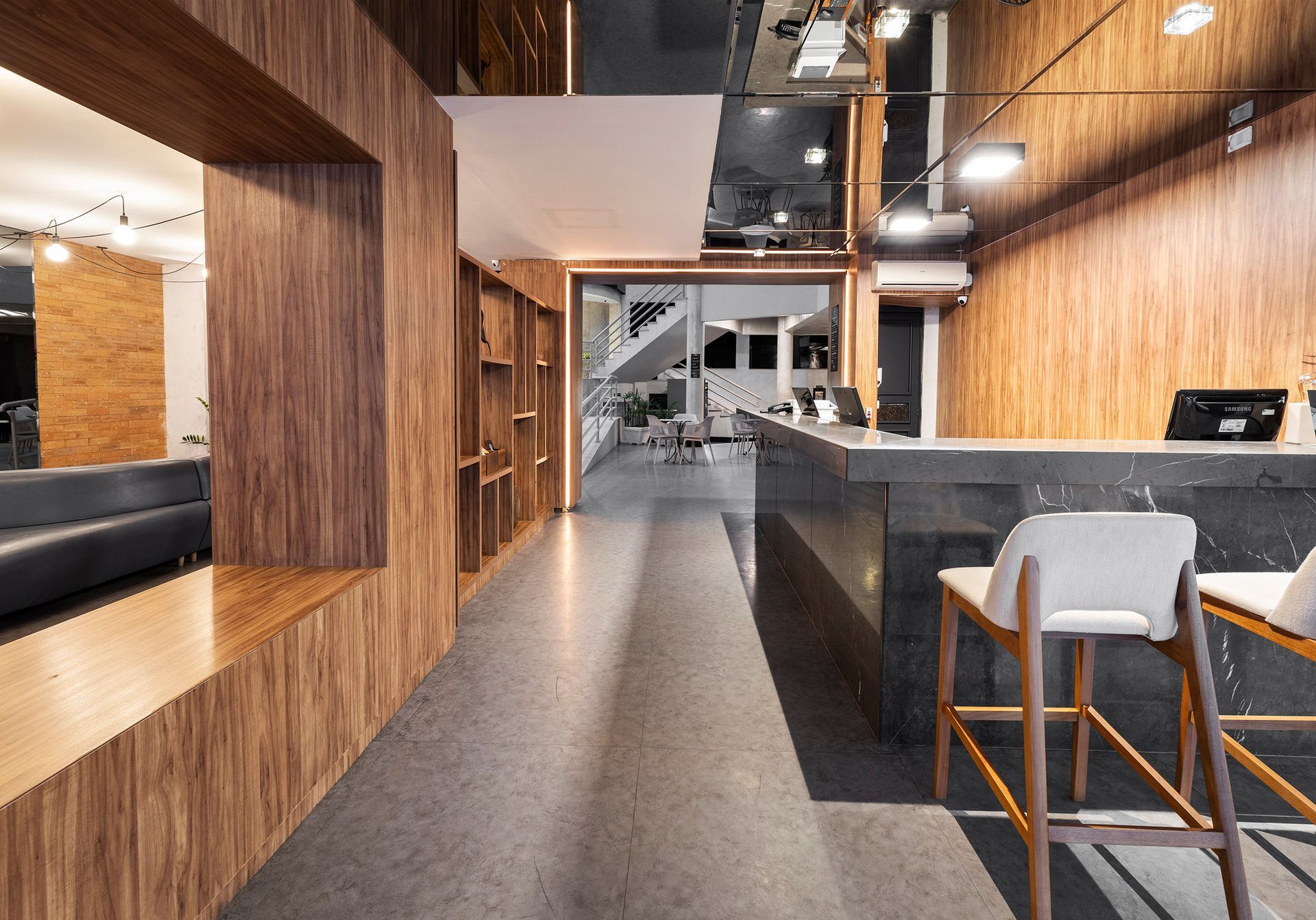 Interior moderno de café, com painéis de madeira, balcões pretos e bancos brancos ao longo de um corredor central