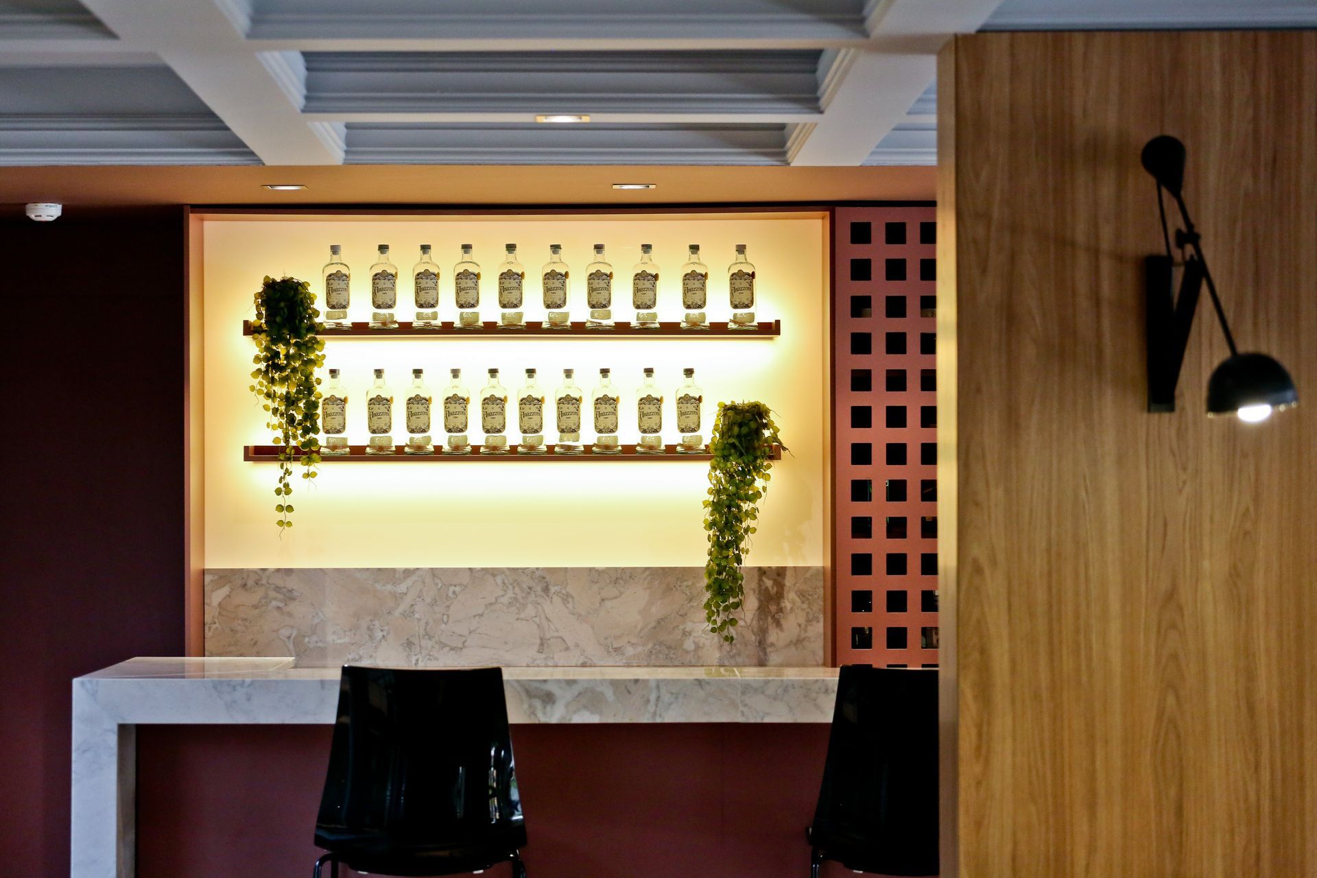 Interior de bar moderno com expositor de bebidas iluminado, banquetas, balcão de mármore e paredes revestidas de madeira