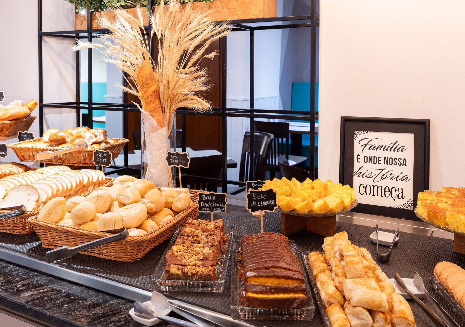 Buffet de sobremesas com doces, muffins e tortas de frutas sobre um balcão preto, com uma placa decorativa e capins secos
