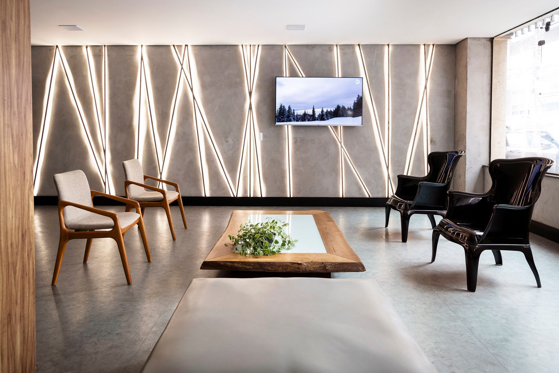 Sala de estar moderna com arandelas esculturais, cadeiras, uma mesa baixa e uma TV montada na parede.