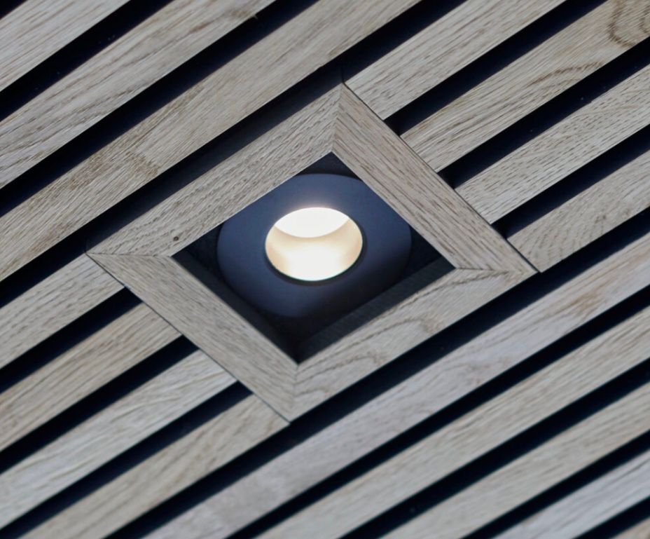 Diagonal wooden slat ceiling with a recessed spotlight framed in wood.