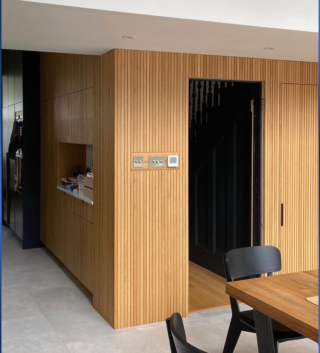 Wooden paneled walls with a doorway, light switches, and a dining table.