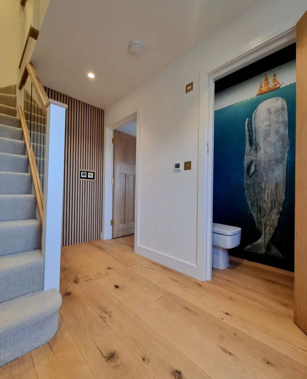 Hallway with wooden floors, stairs, a curtain, and a bathroom with a whale mural.