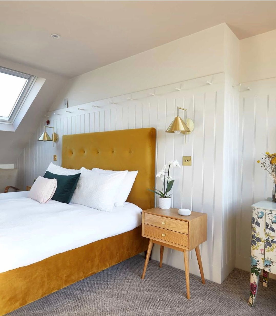 Bedroom with yellow bed, white bedding, nightstand, and floral cabinet.