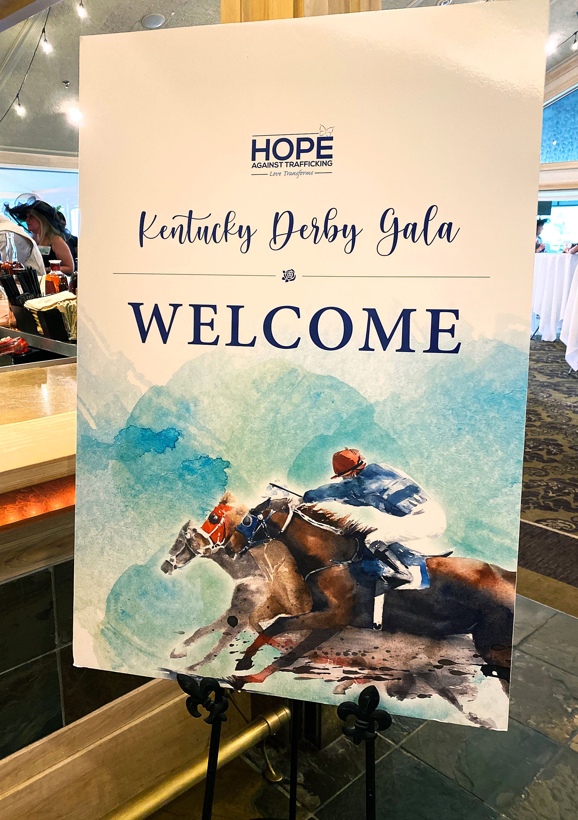 A welcome sign for a derby gala with a picture of horses and jockeys.