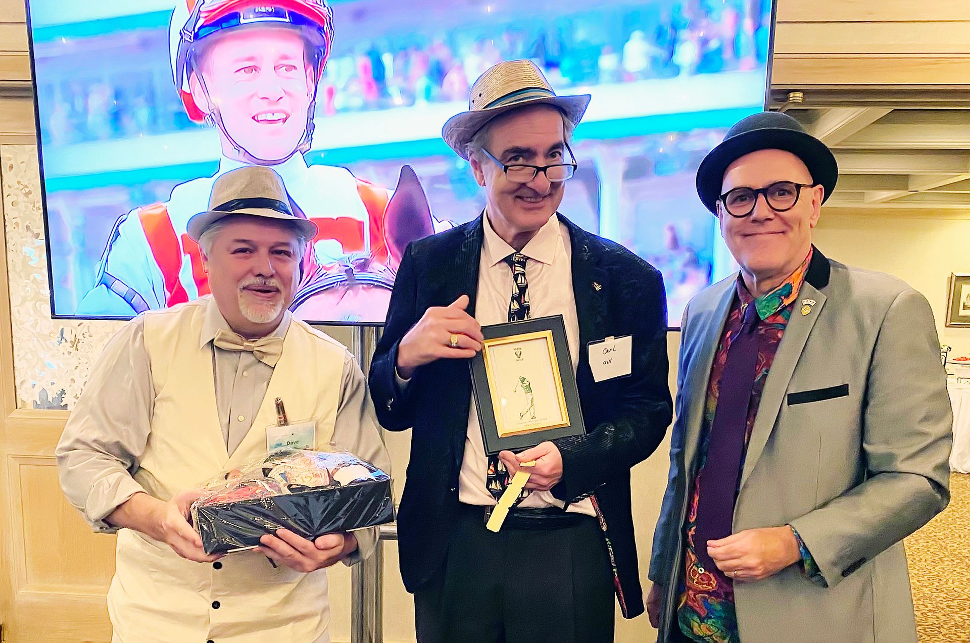 Three men are standing next to each other in front of a large screen.