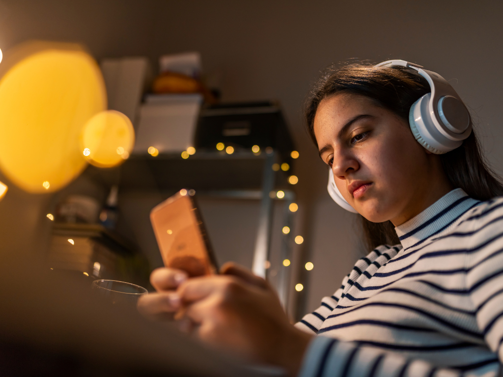 A teenager wearing headphones is looking at her phone.
