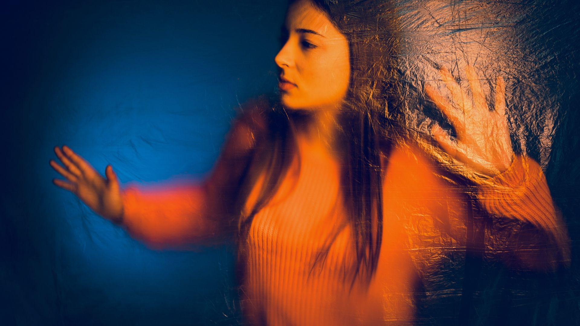 A woman in an orange sweater is standing behind a glass door.