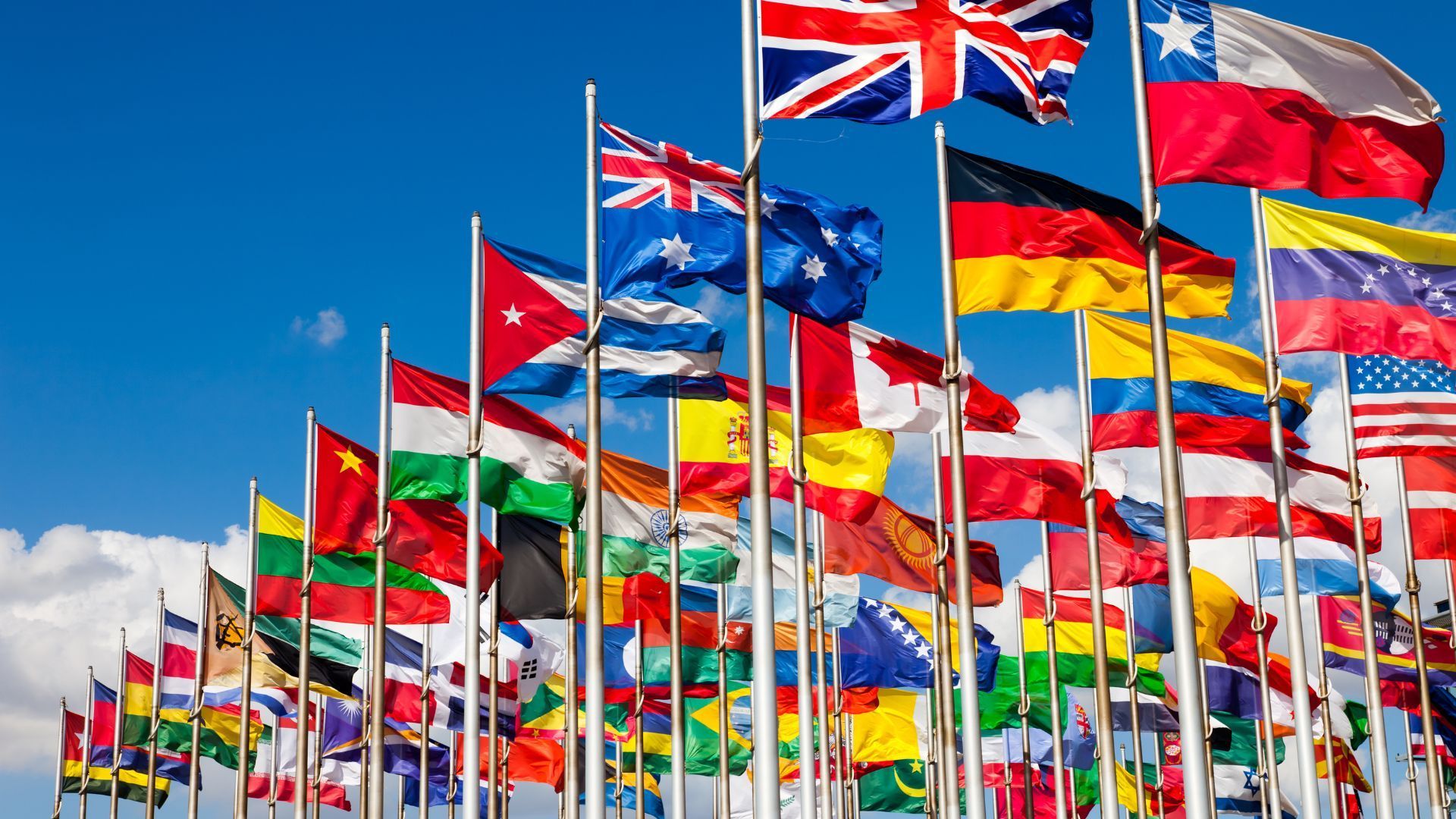 A bunch of flags from different countries are flying in the wind.