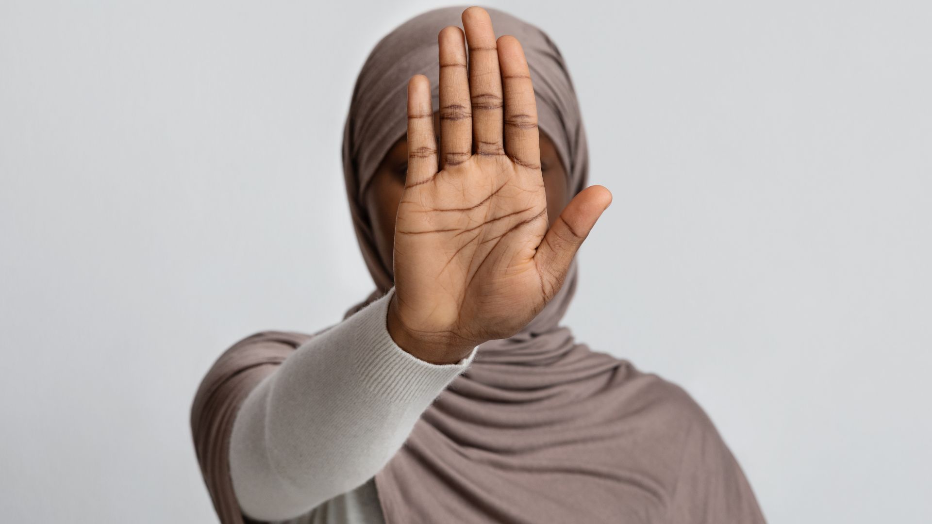 A woman in a hijab is covering her face with her hand.