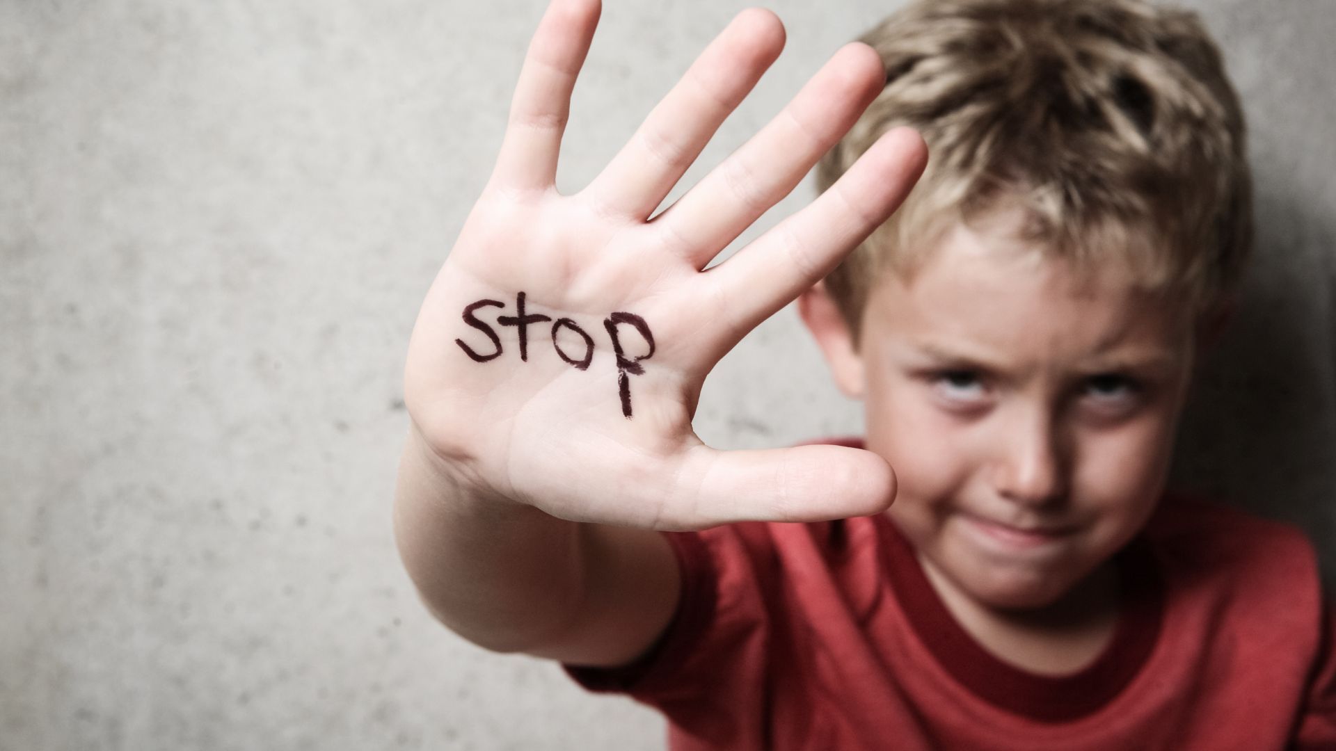 A young boy holds up his hand with the word stop written on it