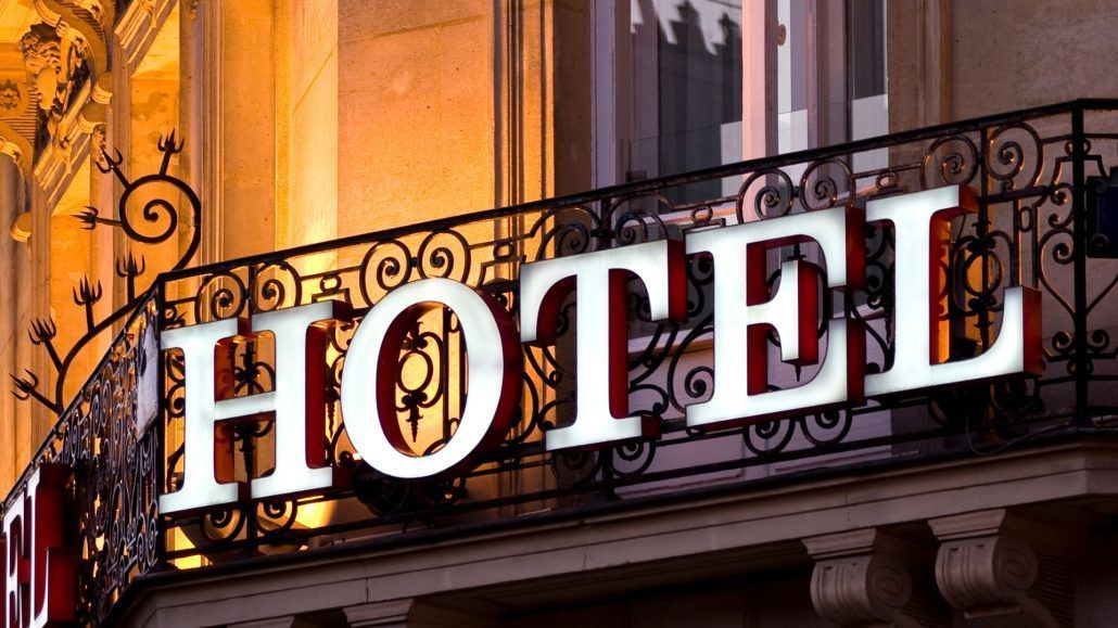 Large white “HOTEL” sign on a wrought-iron balcony against a warm lit building facade.