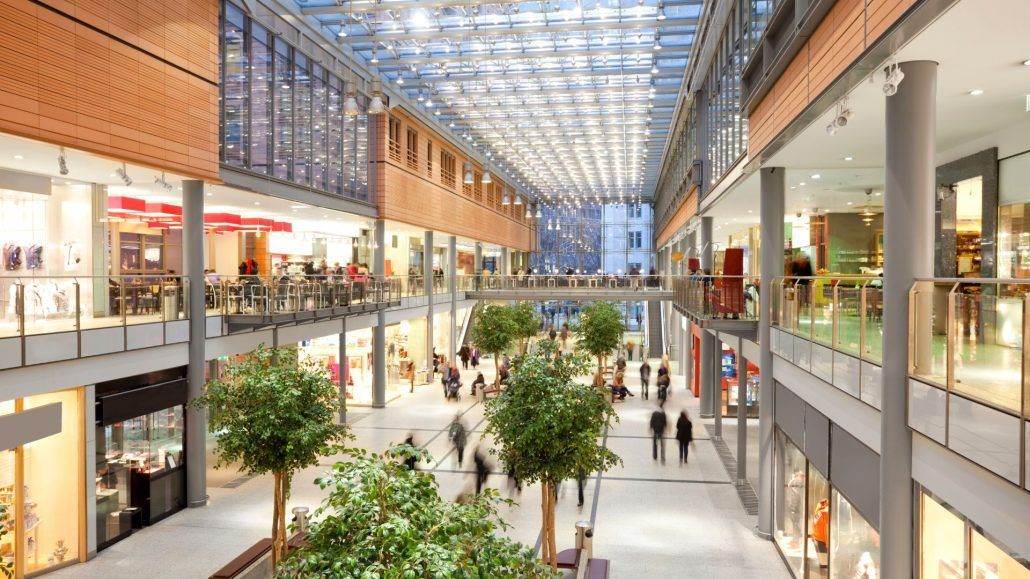 Bright indoor shopping mall with skylit ceiling, storefronts, and a few people walking through the atrium