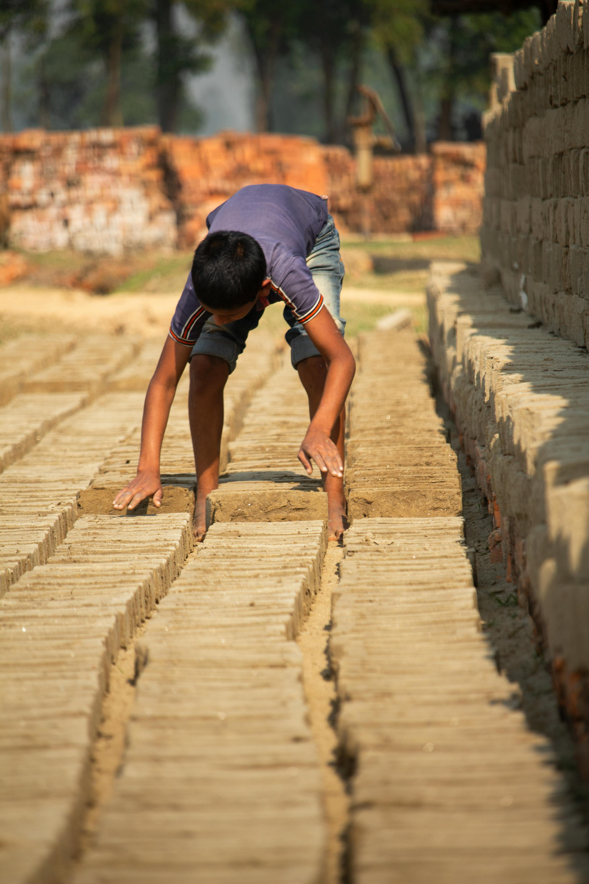 A young boy is bending over a row of bricks.