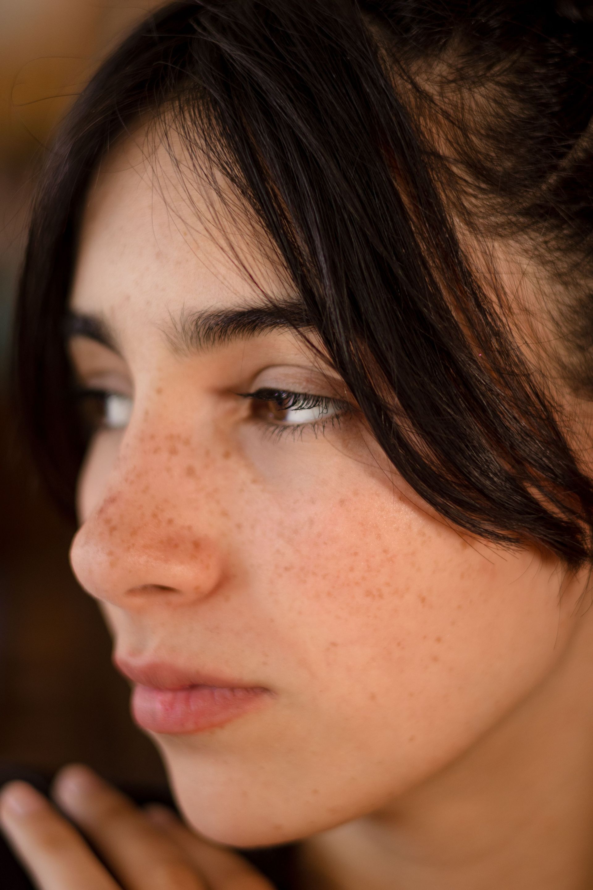 Close-up profile of a person with dark hair and freckles, looking left with a neutral expression