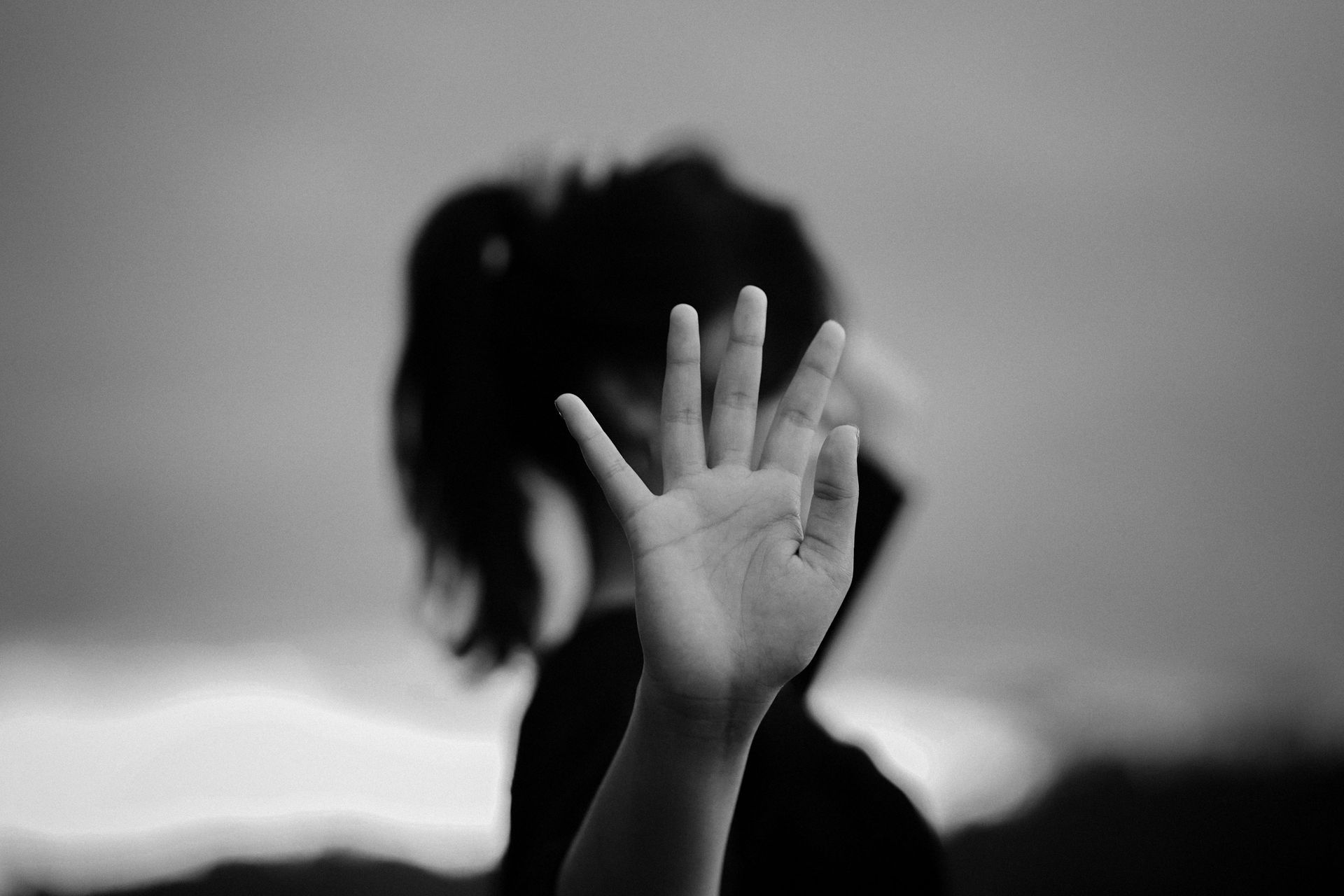 Silhouetted person with raised hand blocking their face against a blurred gray sky