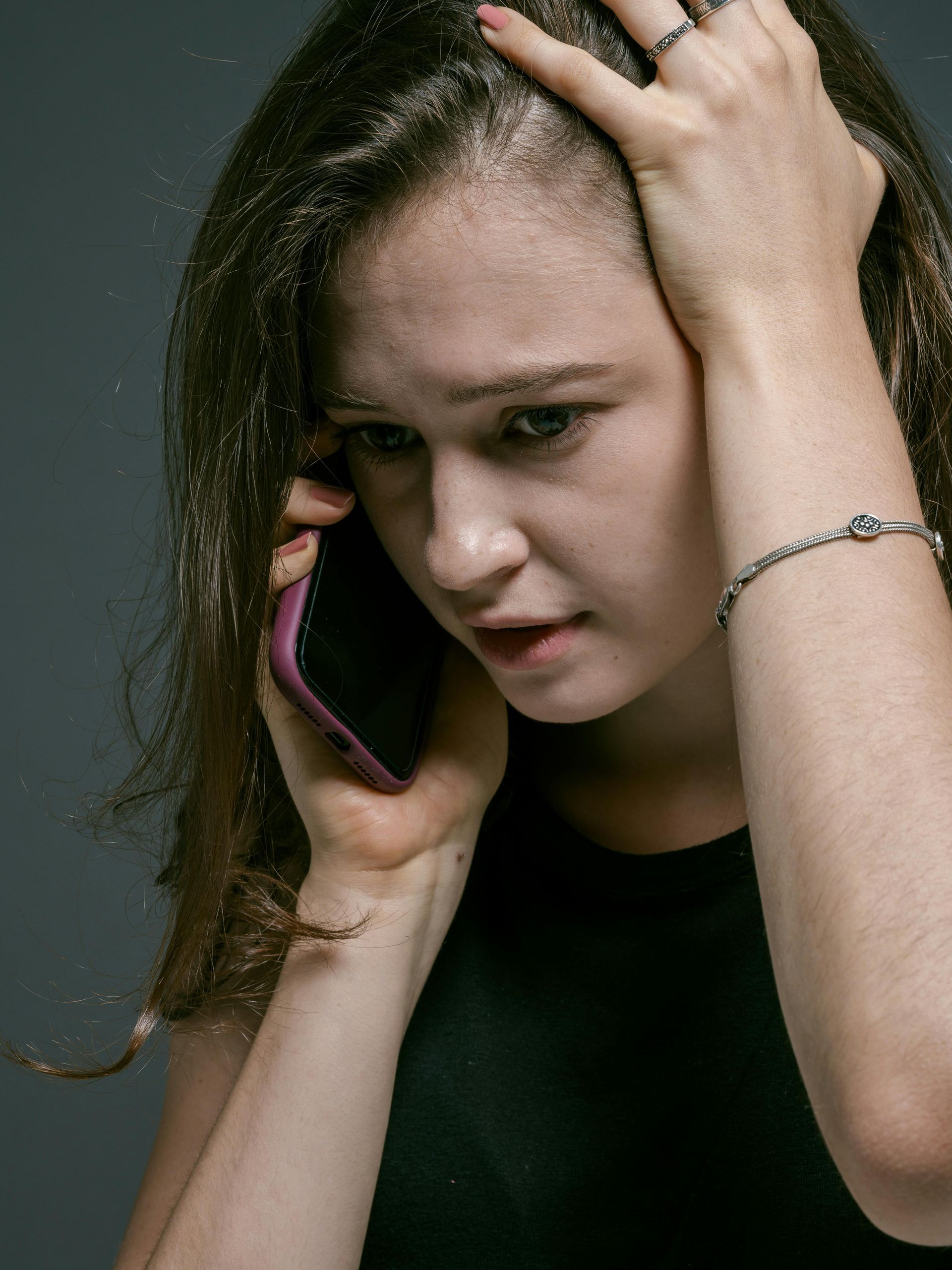 A woman is holding her head while talking on a cell phone.