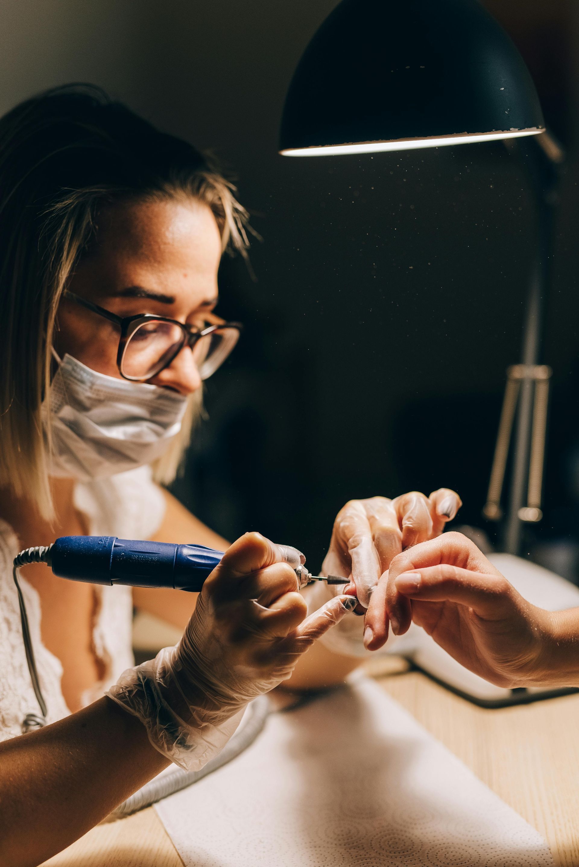 A woman is wearing a mask and gloves while getting her nails done.