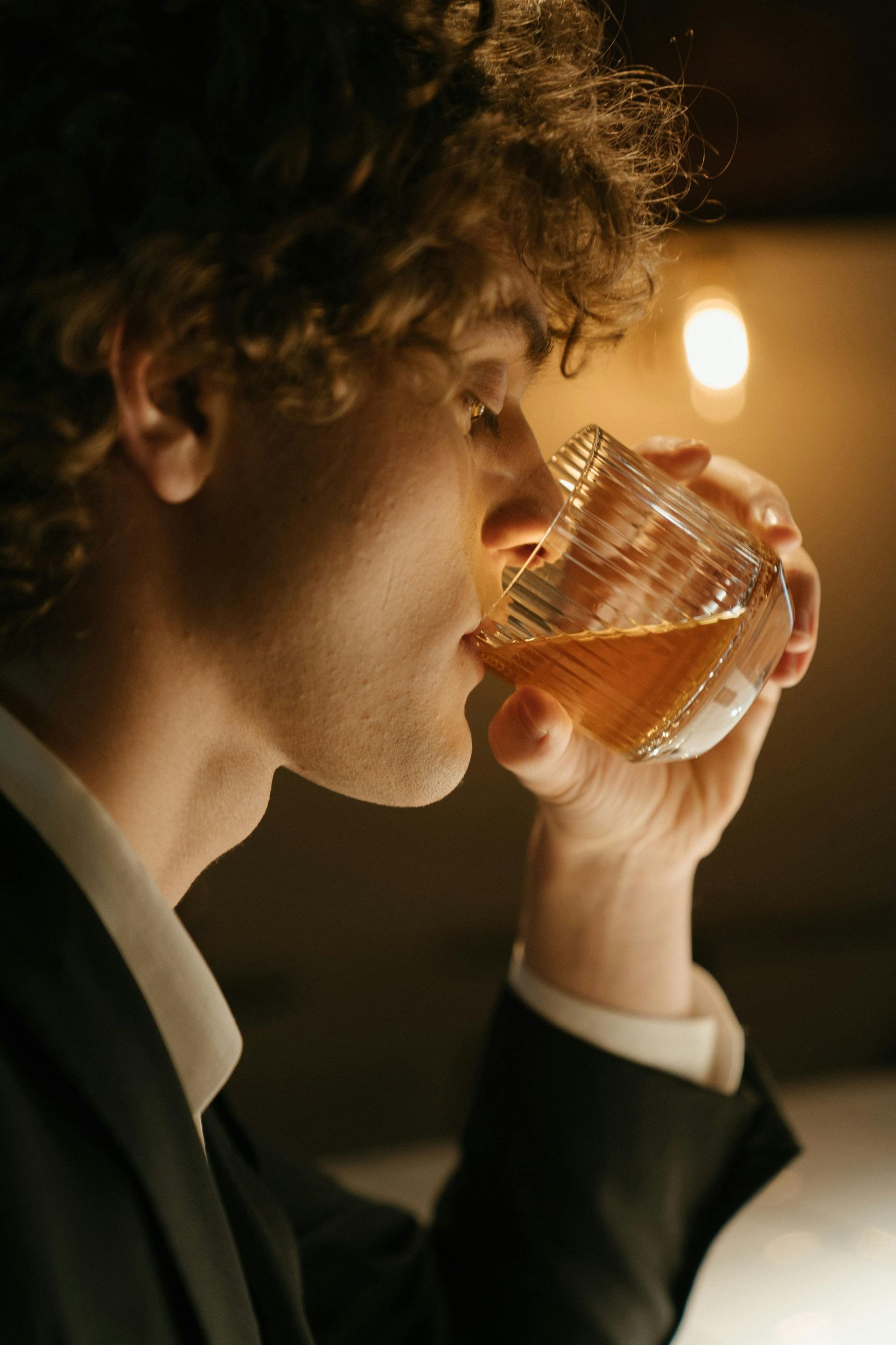 A man in a suit is drinking a glass of whiskey.