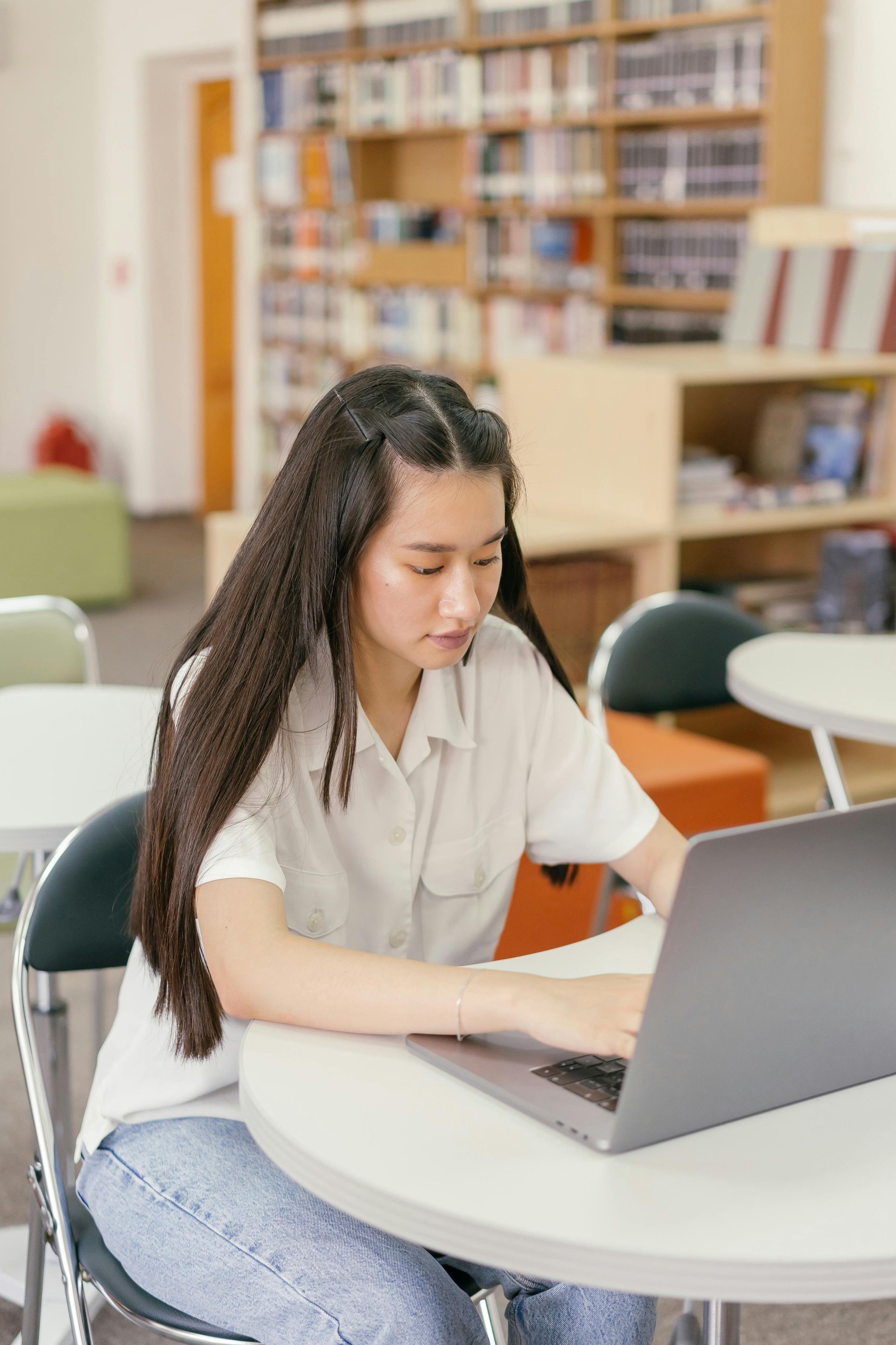 A woman is sitting at a table using a laptop computer in a library.
