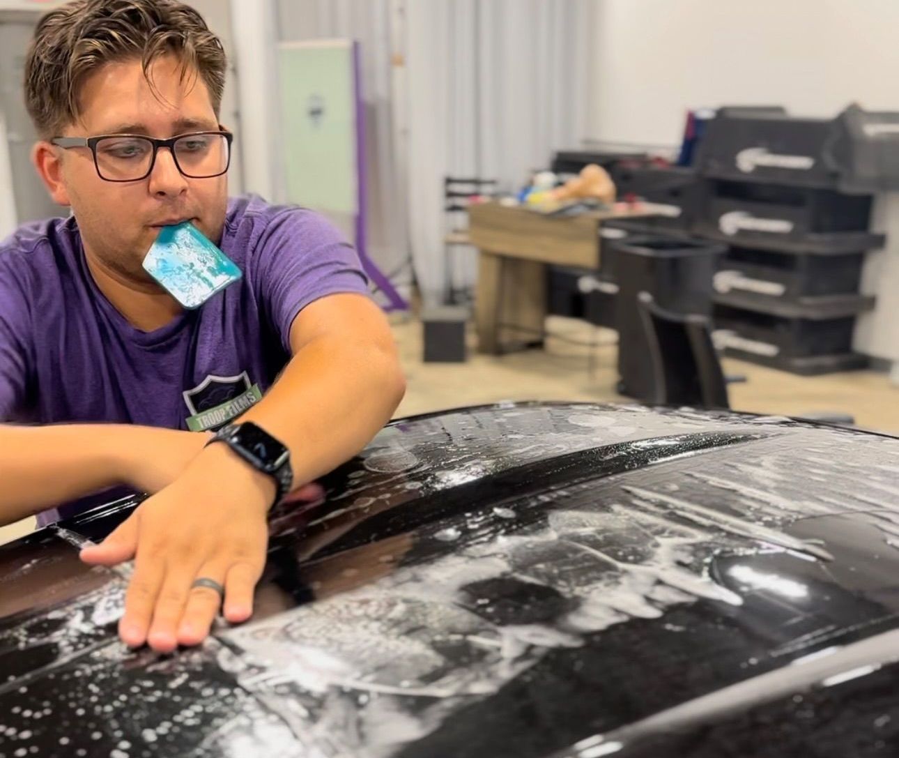a man in a purple shirt is sitting on the hood of a car