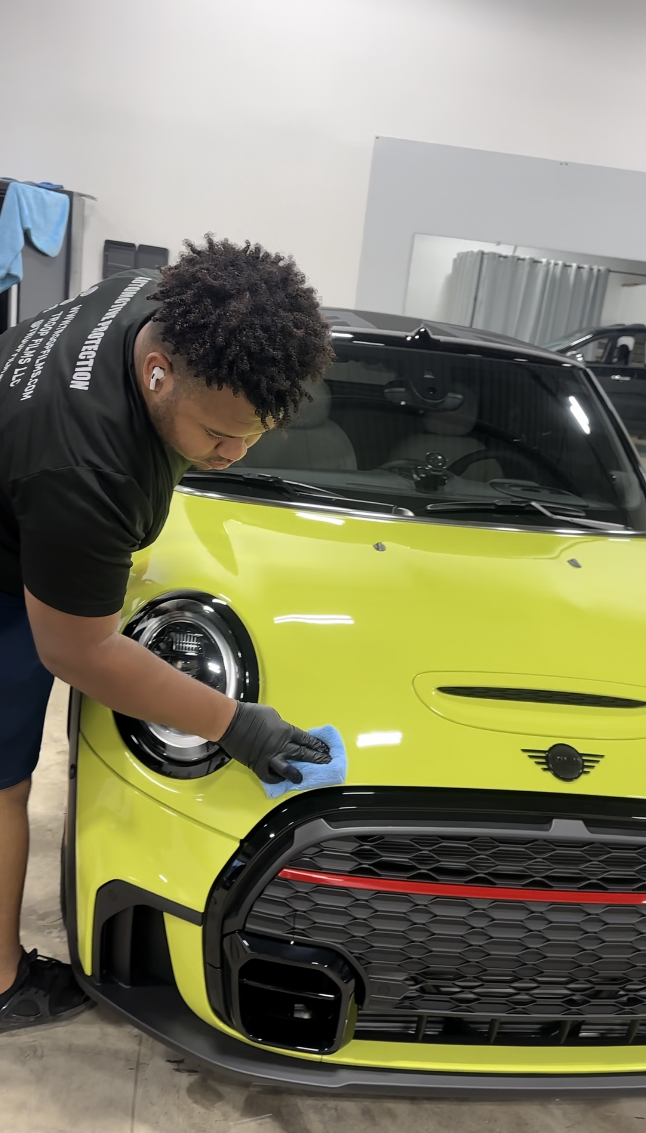 a man is cleaning the front of a yellow mini cooper .