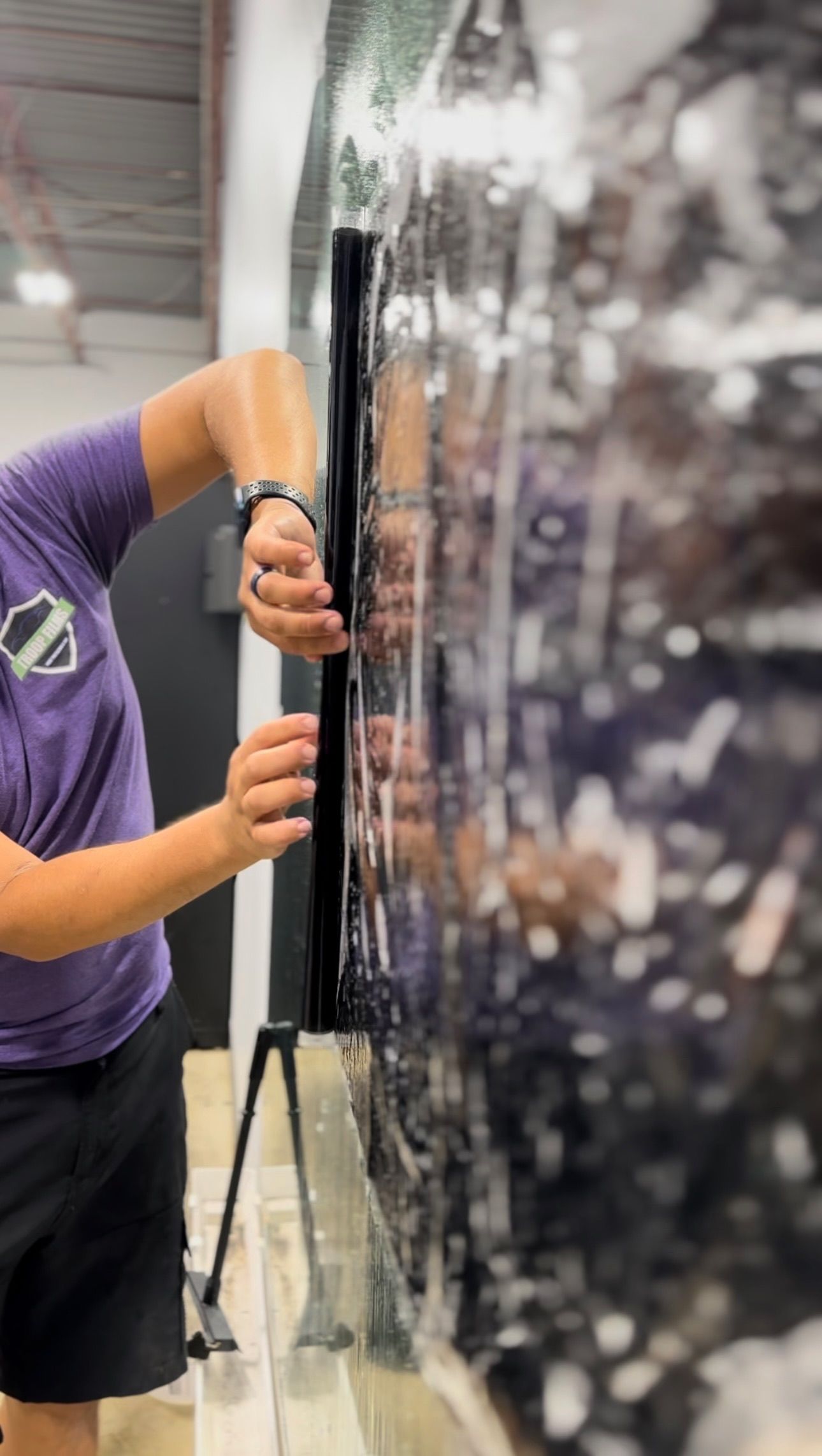 Person applying film to a window. They are holding a straight edge tool, appearing to squeegee the film.