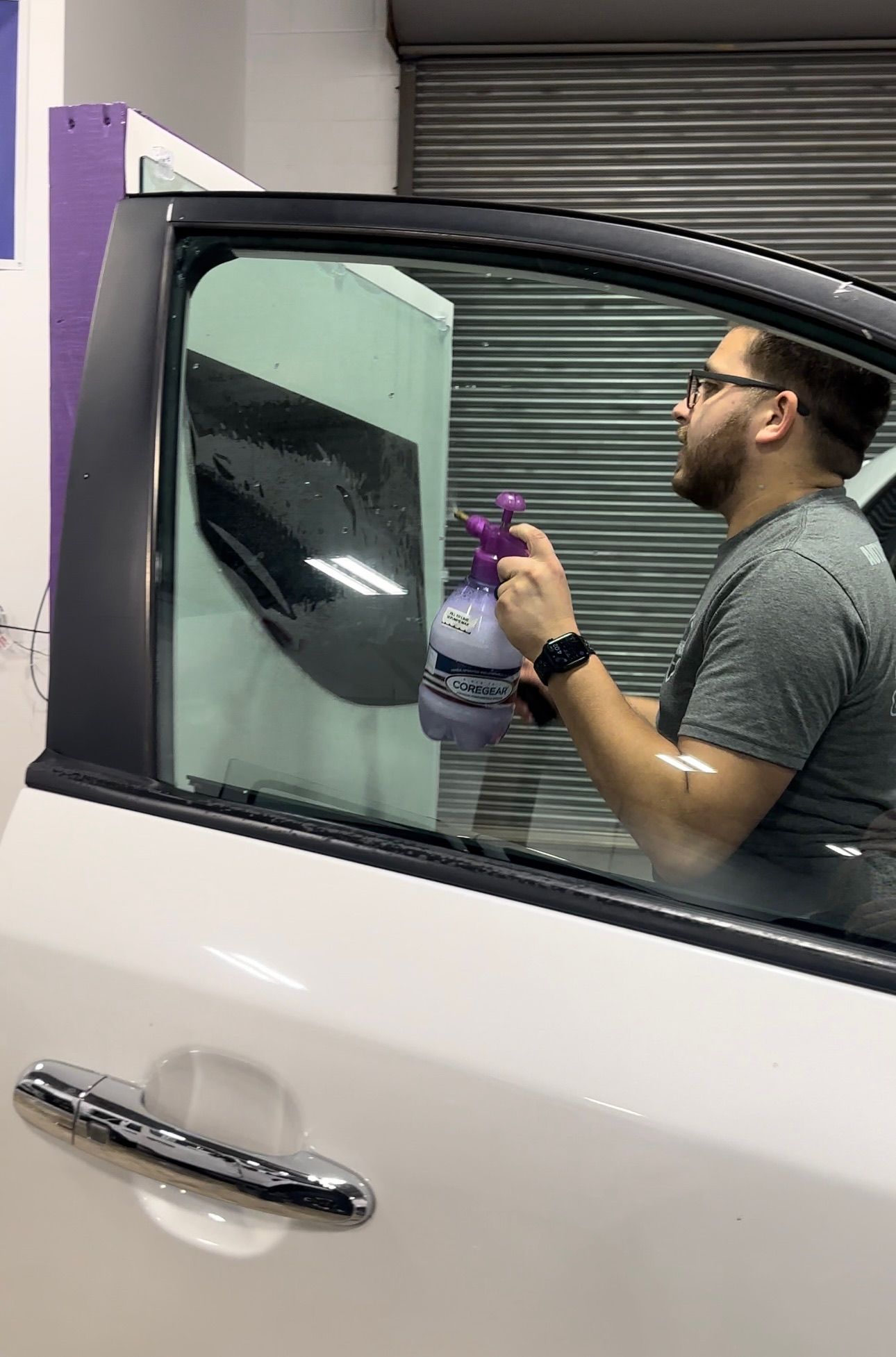 Man spraying a car window with a bottle of liquid. Garage setting.