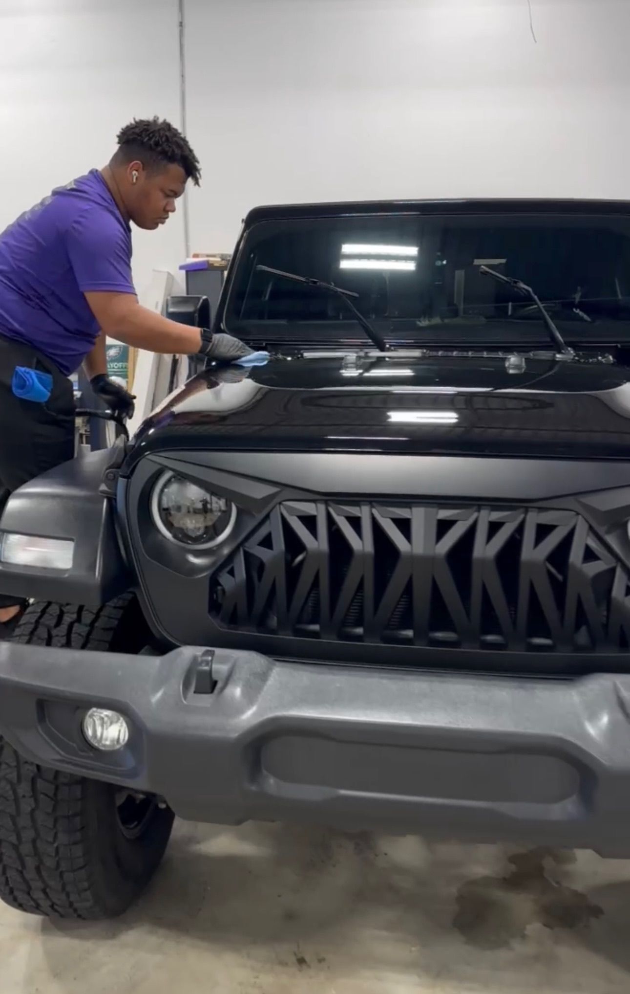 Person cleaning the hood of a black Jeep. The person wears a purple shirt and black gloves.