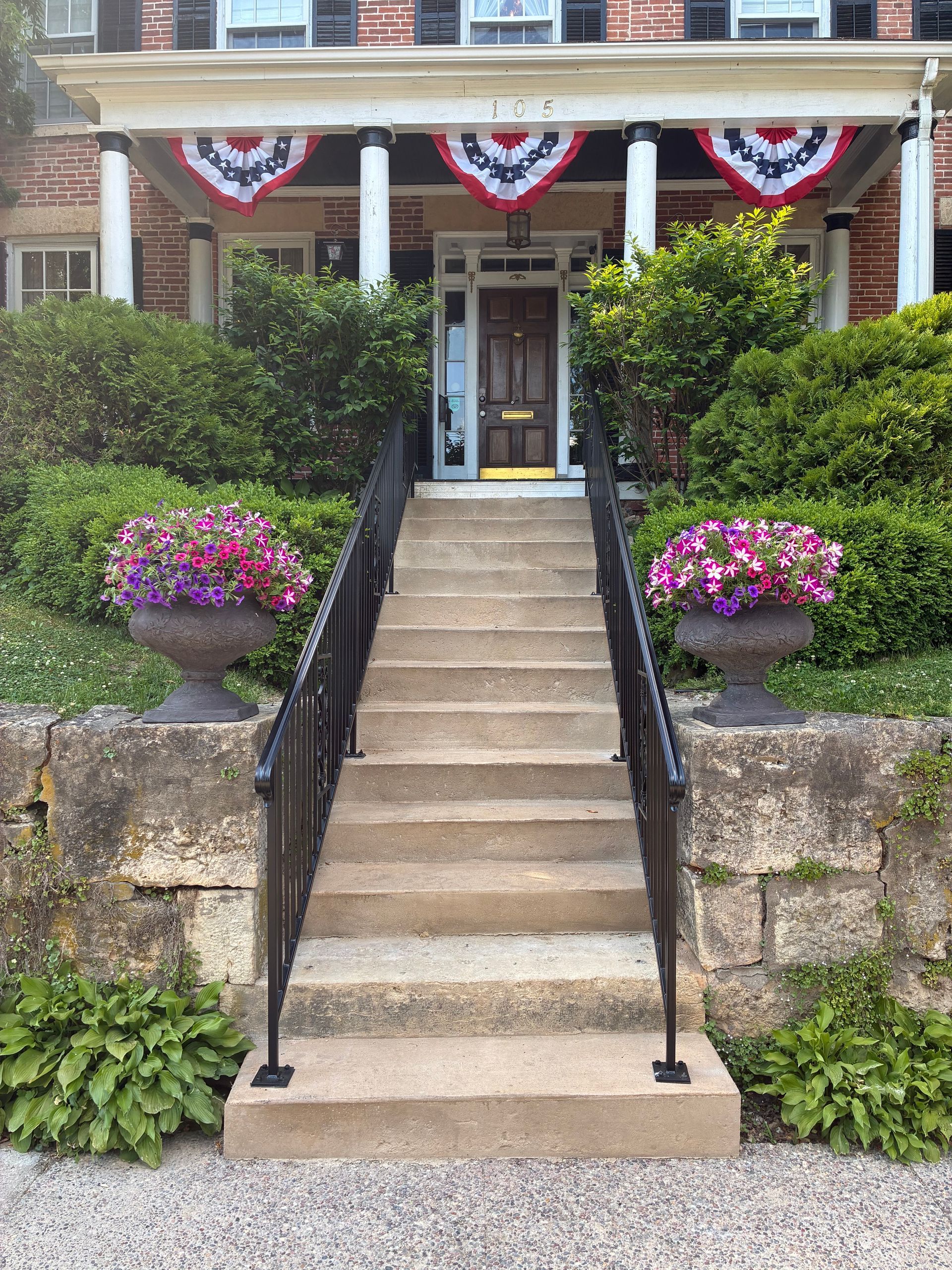 Brick house with white columns, front door, and manicured landscaping.